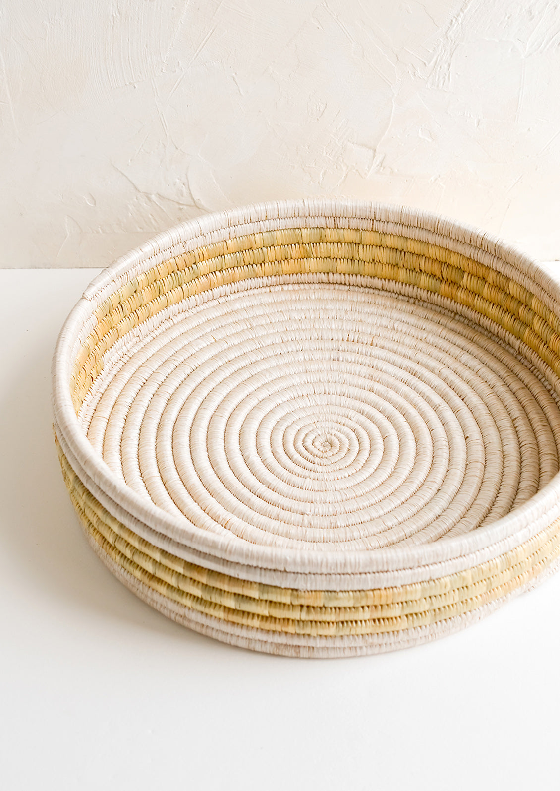 A round, shallow woven seagrass tray in white and beige.