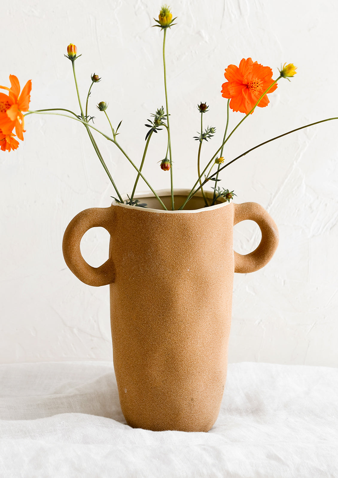A tall brown ceramic vase with orange cosmos.