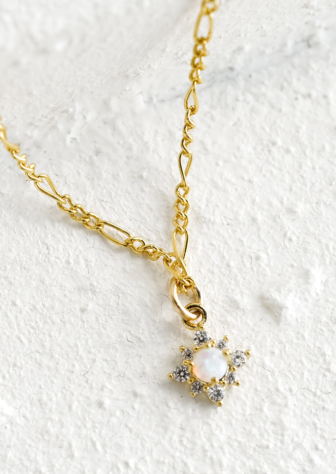A gold figaro chain necklace with opal and crystal north star pendant.