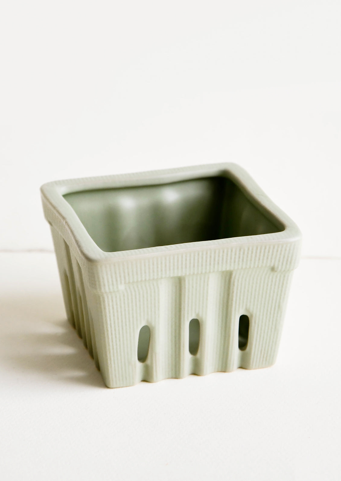 Ceramic basket in the style of disposable berry basket, shown in sage green