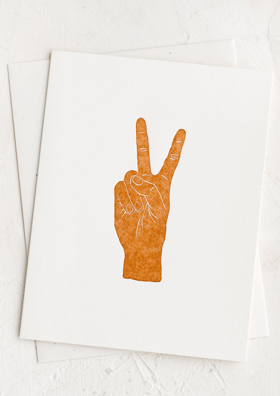 A white card with brown letter pressed hand doing a peace sign.