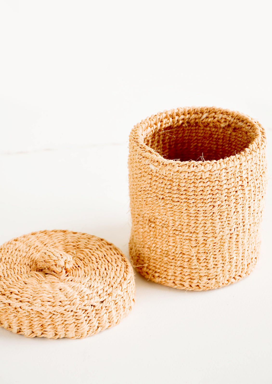 Small, round woven basket with matching lid made from peach-colored sisal