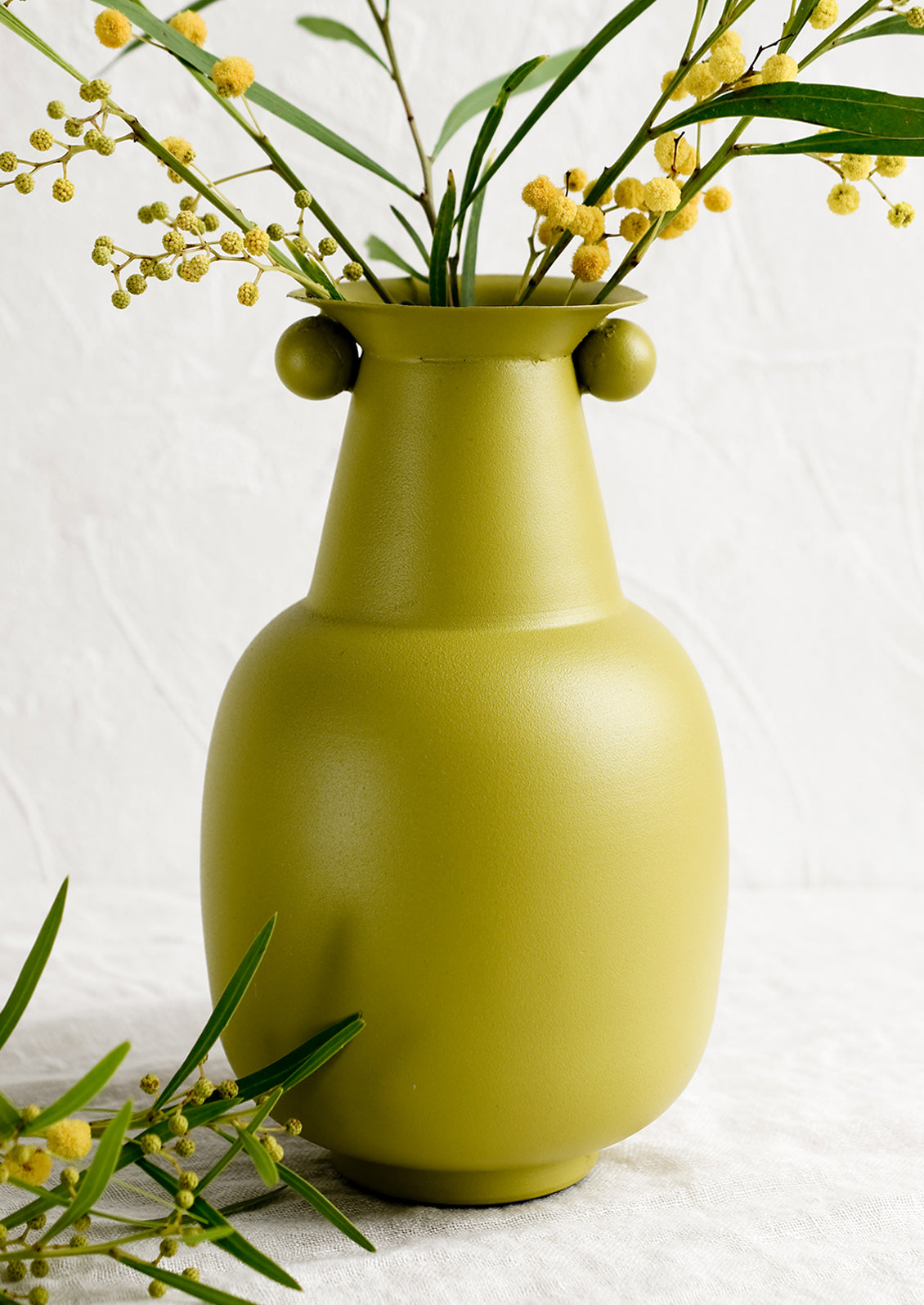 A lime green vase with mimosa flowers.