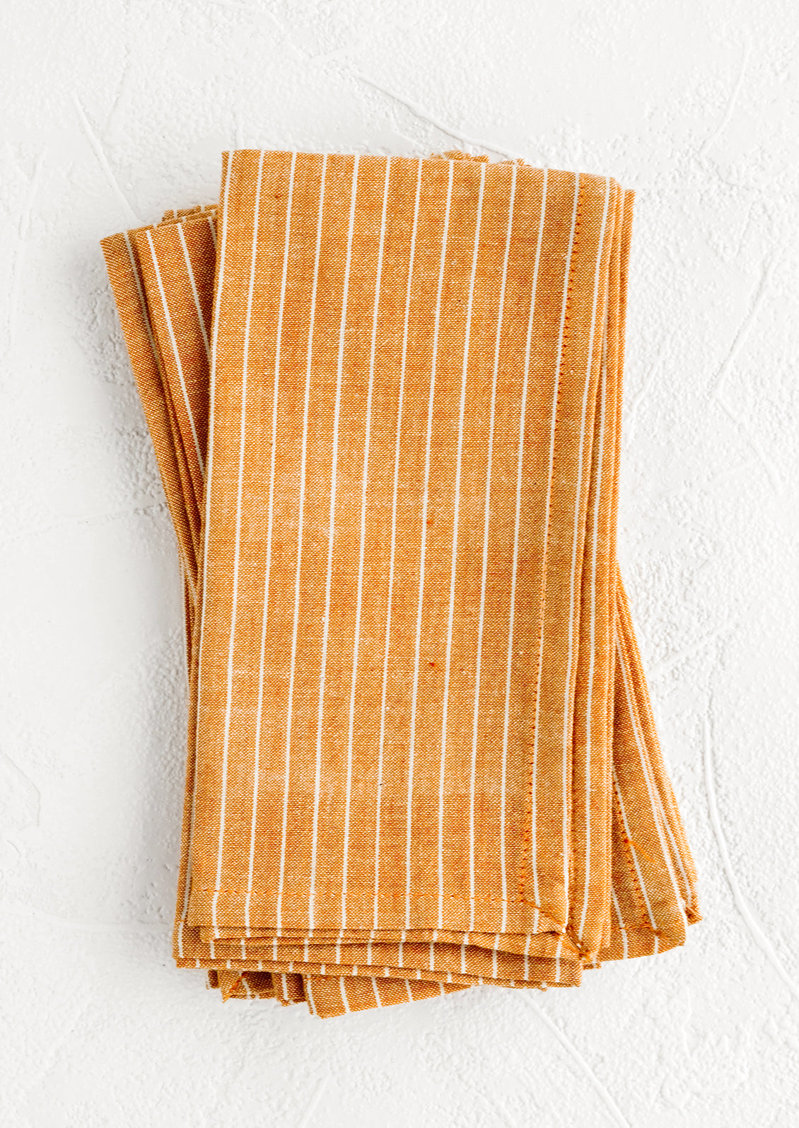 Folded fabric napkins in a pile featuring orange and white pinstripe pattern.