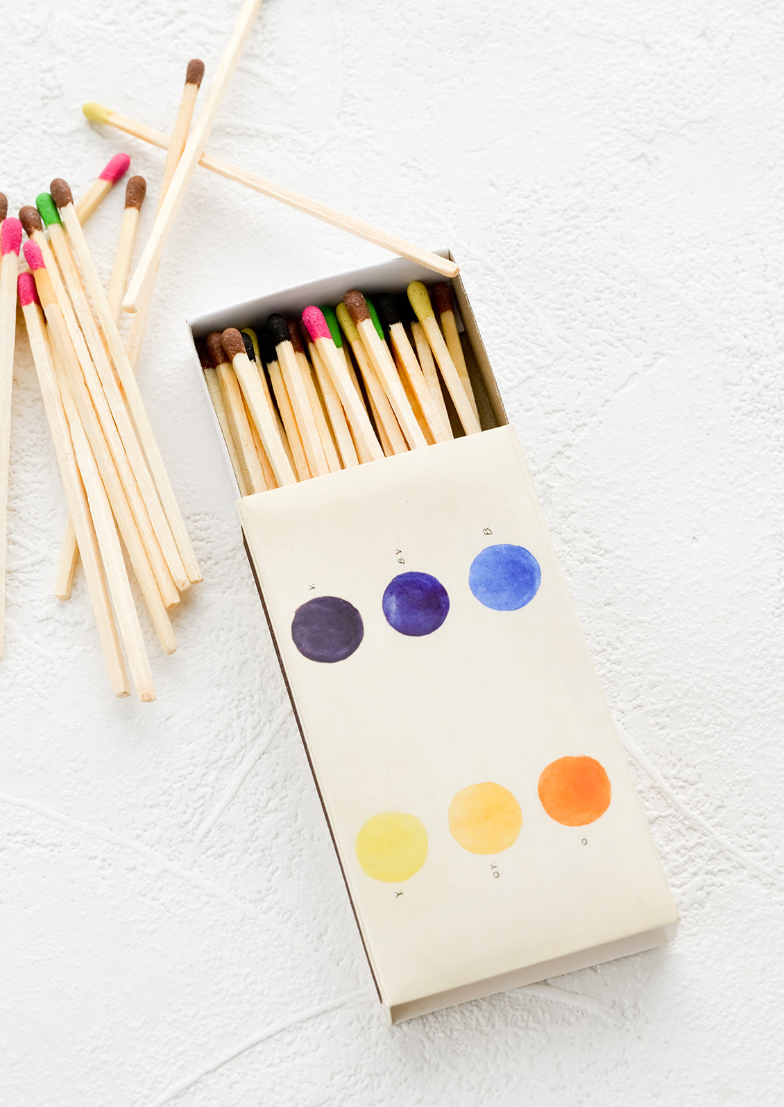 A printed matchbox with color swatches image and matches with colorful tips.