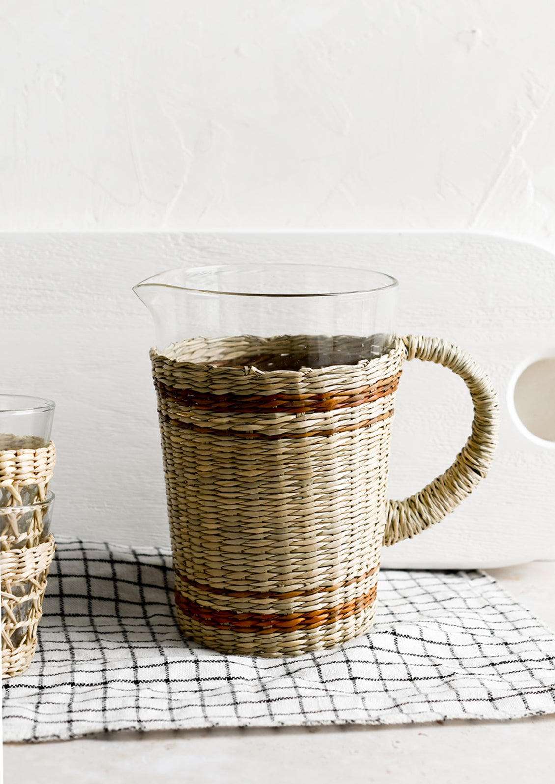 A glass pitcher with striped seagrass cloak and handle.