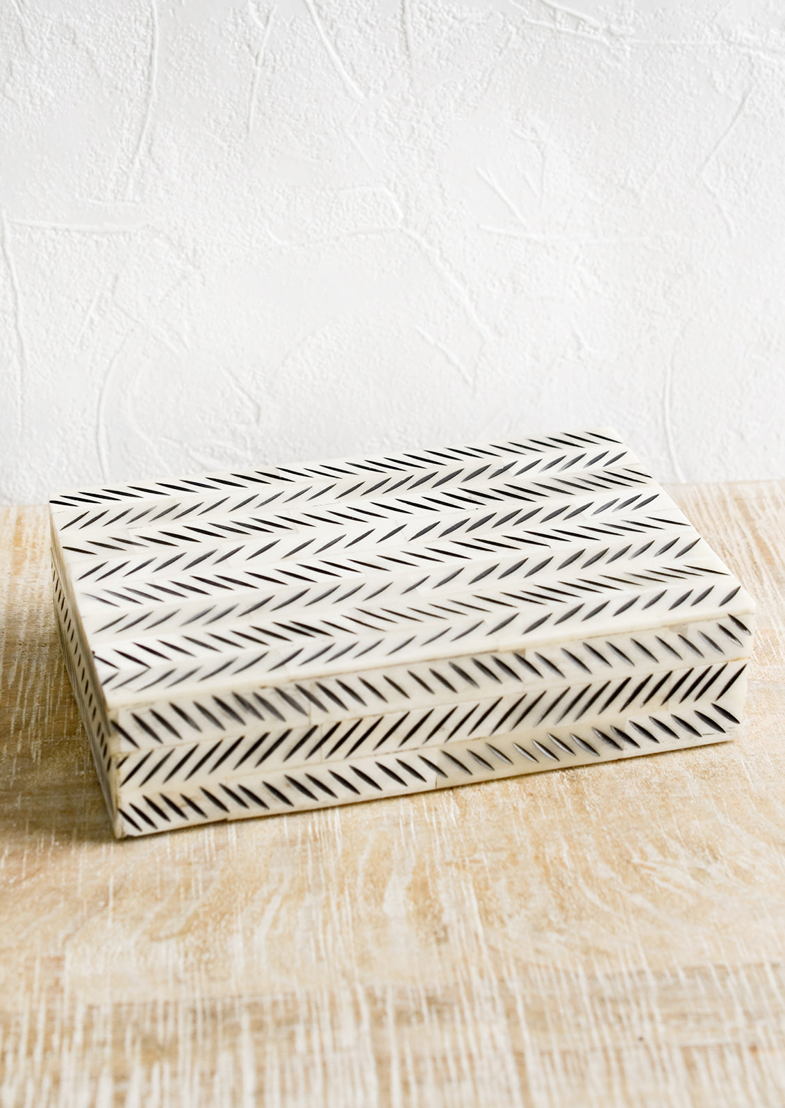 A decorative storage box made from ivory bone with black etched "slash" pattern.