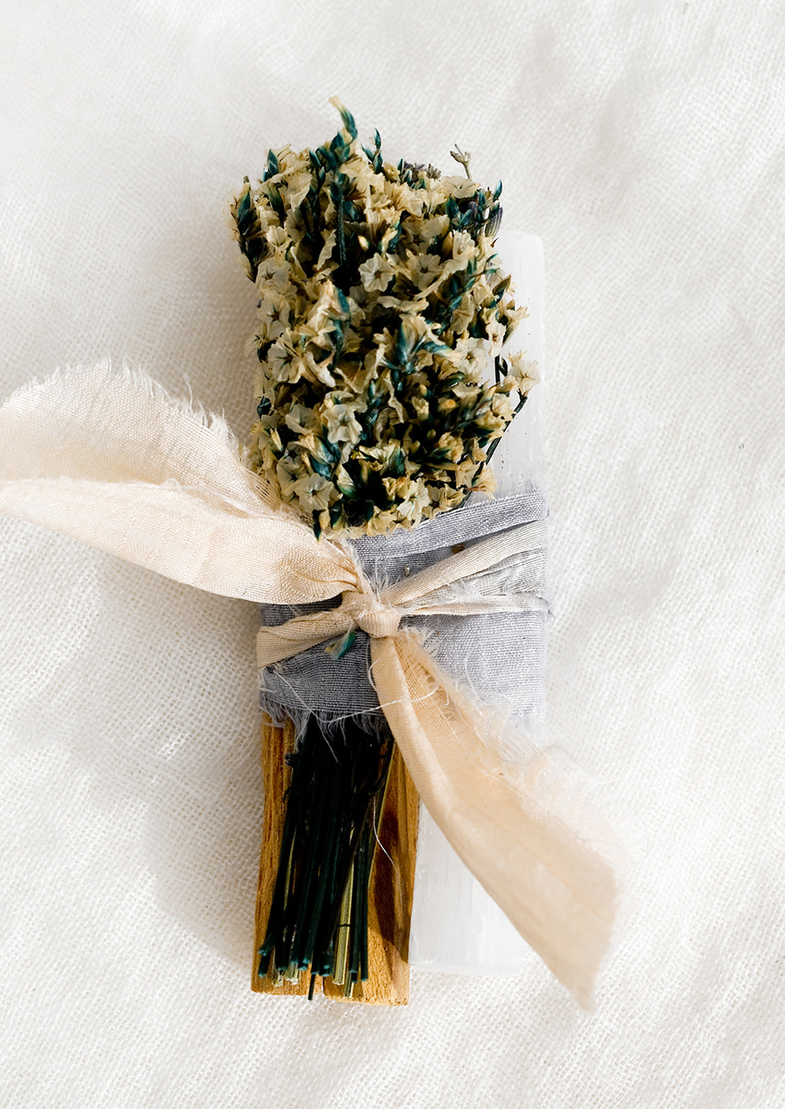A silk ribbon bound bundle of palo santo, dried flowers and selenite.