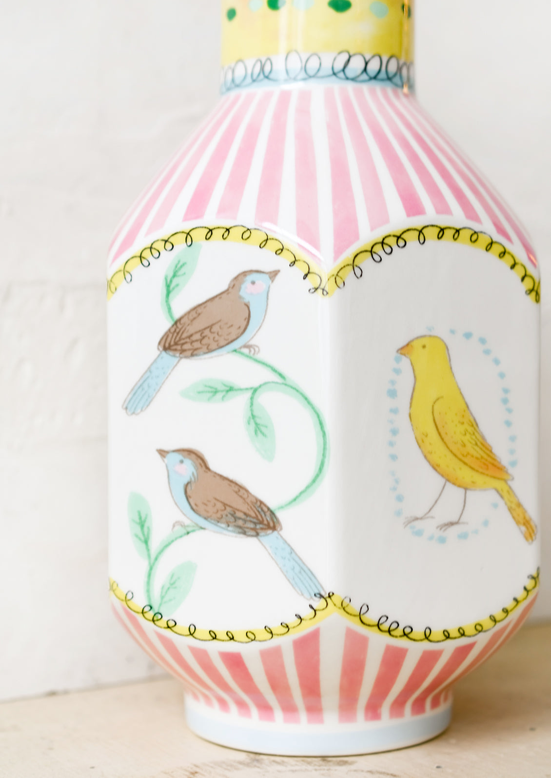 A graphic print vase with pink stripes and three-dimensional shape with bird motif.