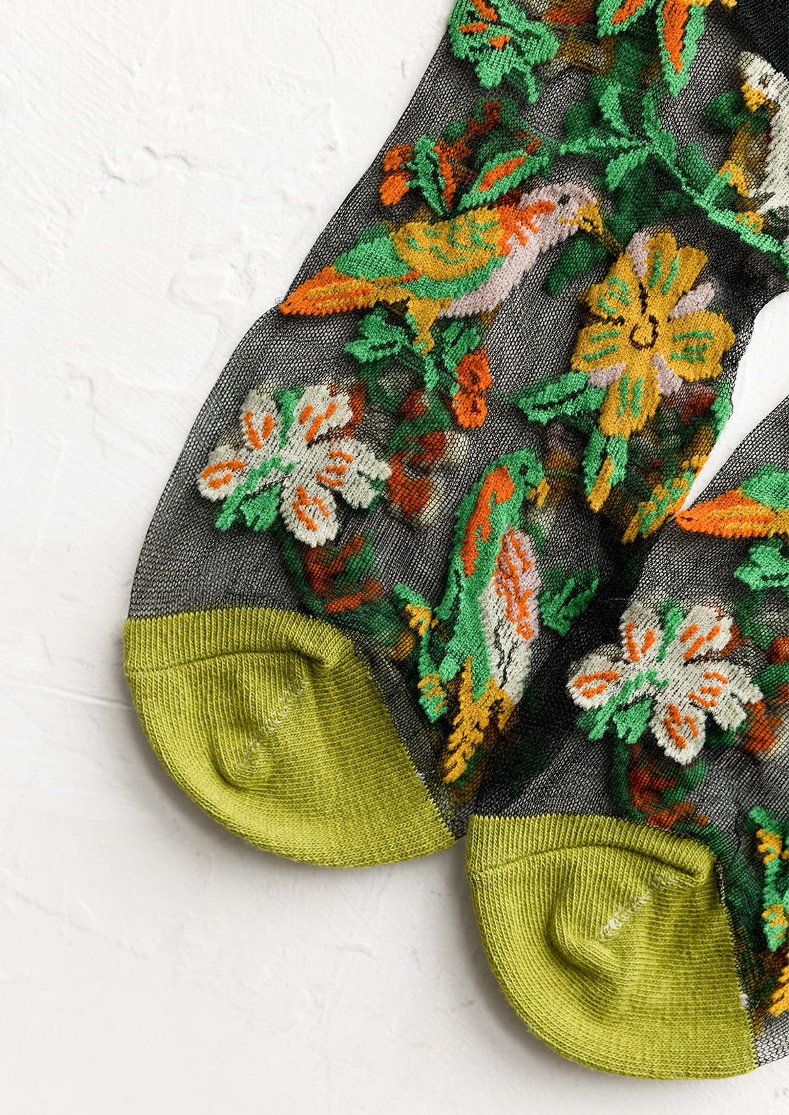 A pair of sheer black socks with tropical parrot print and green toe.
