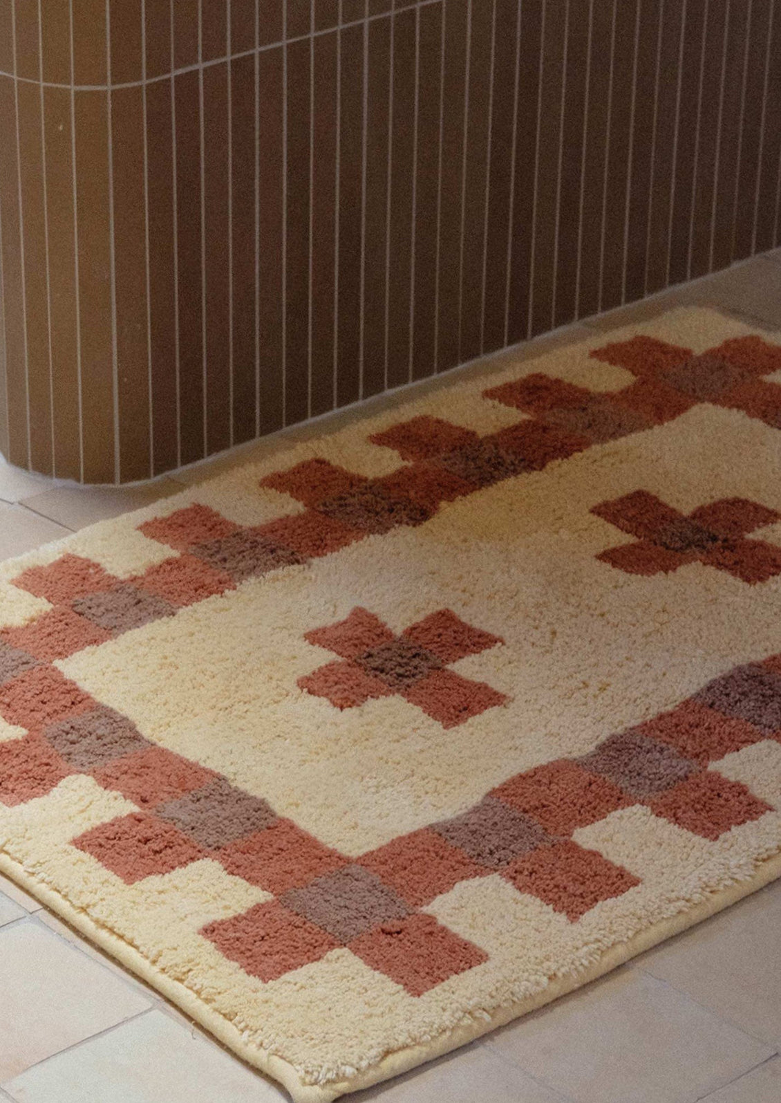 A bath mat in geometric cross print in peach, terracotta and brown.