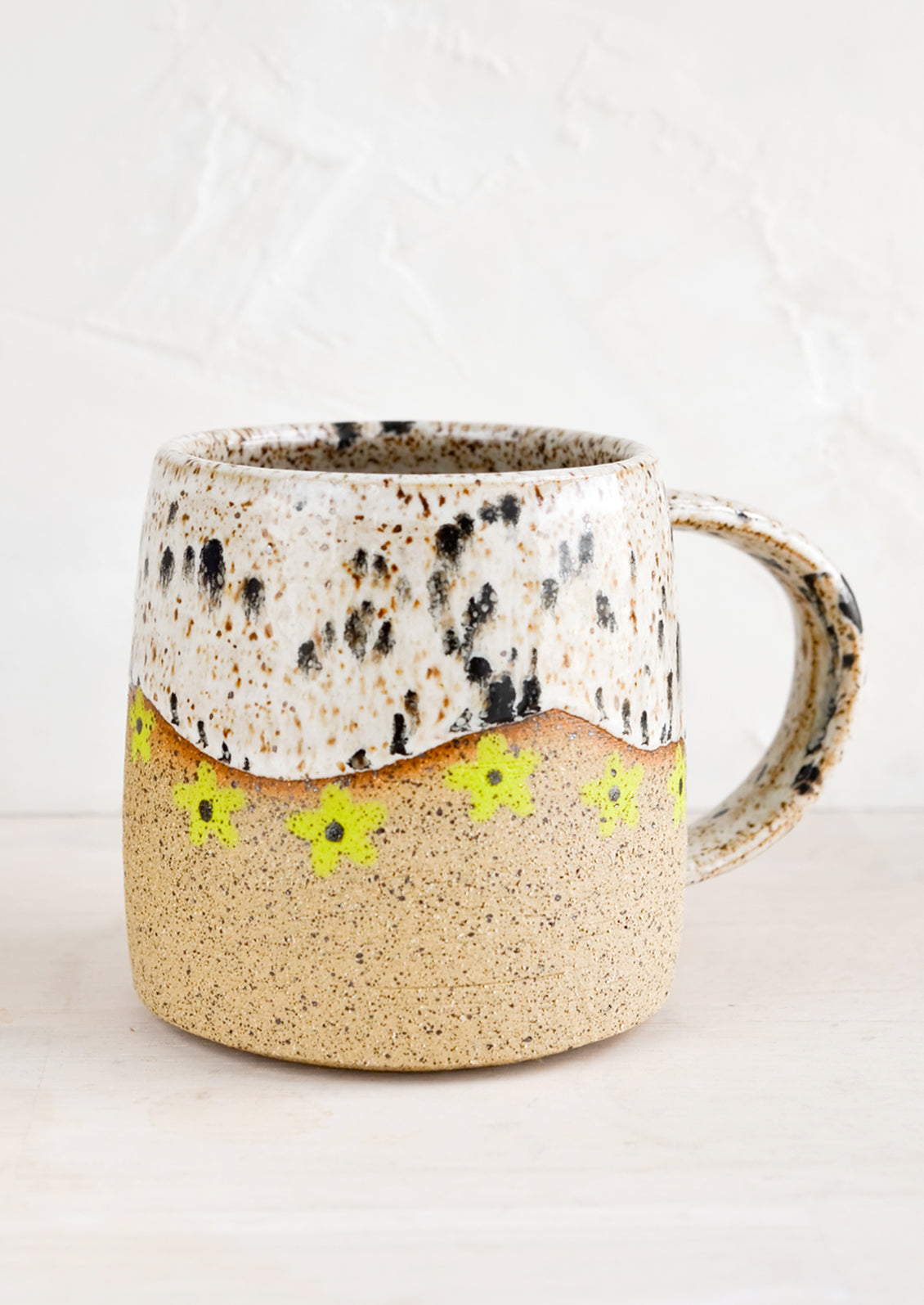 A speckled ceramic coffee mug in black and white with wavy line of lime green daisies at middle.