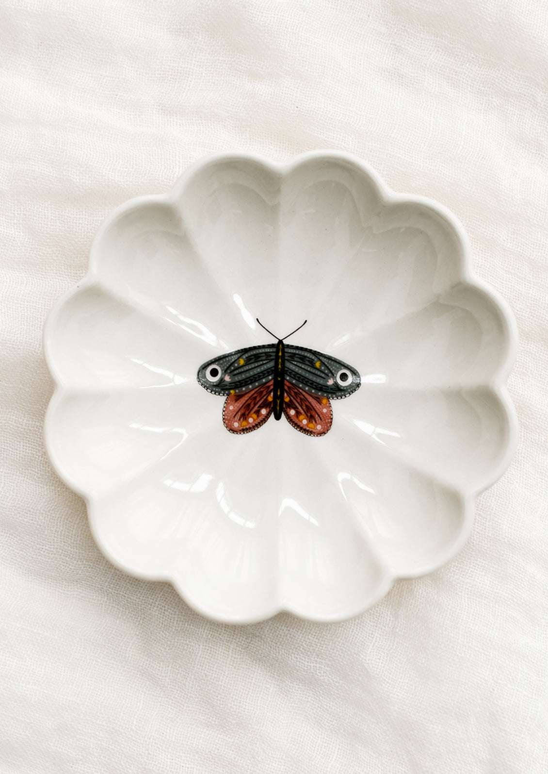 A white ceramic dish with scalloped shape and pink and grey moth illustration at center.