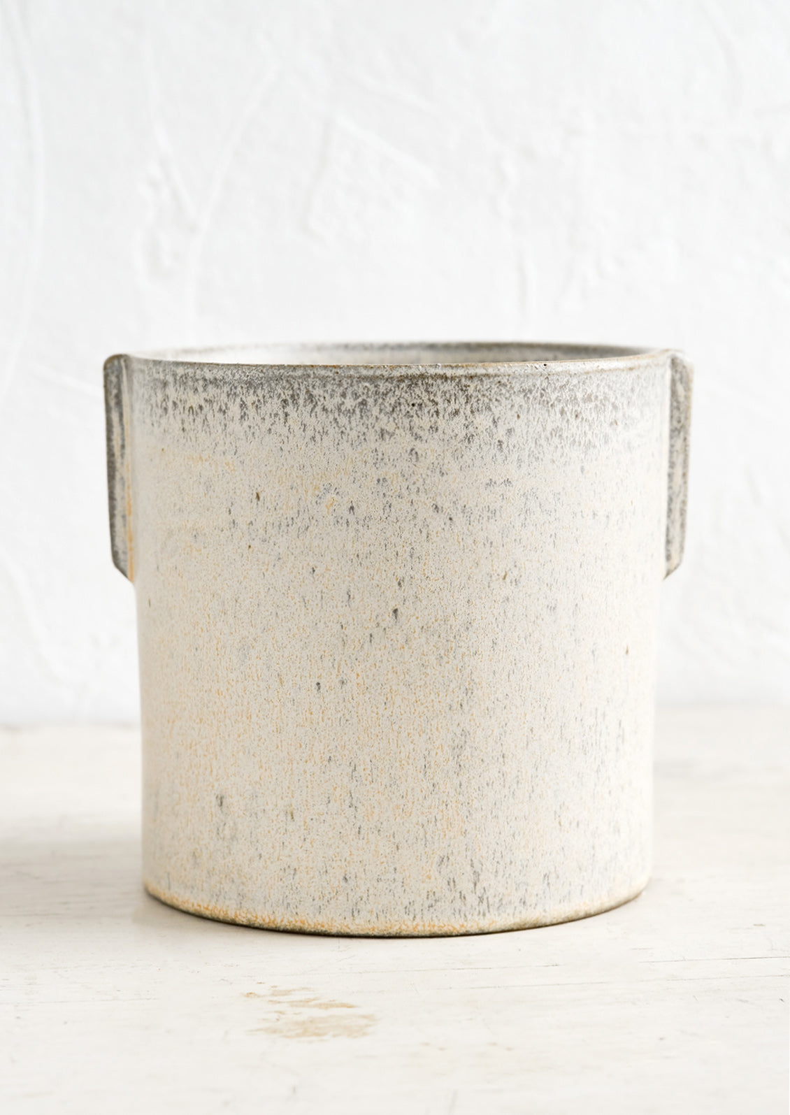 A neutral, speckled ceramic round planter with raised detailing at sides.