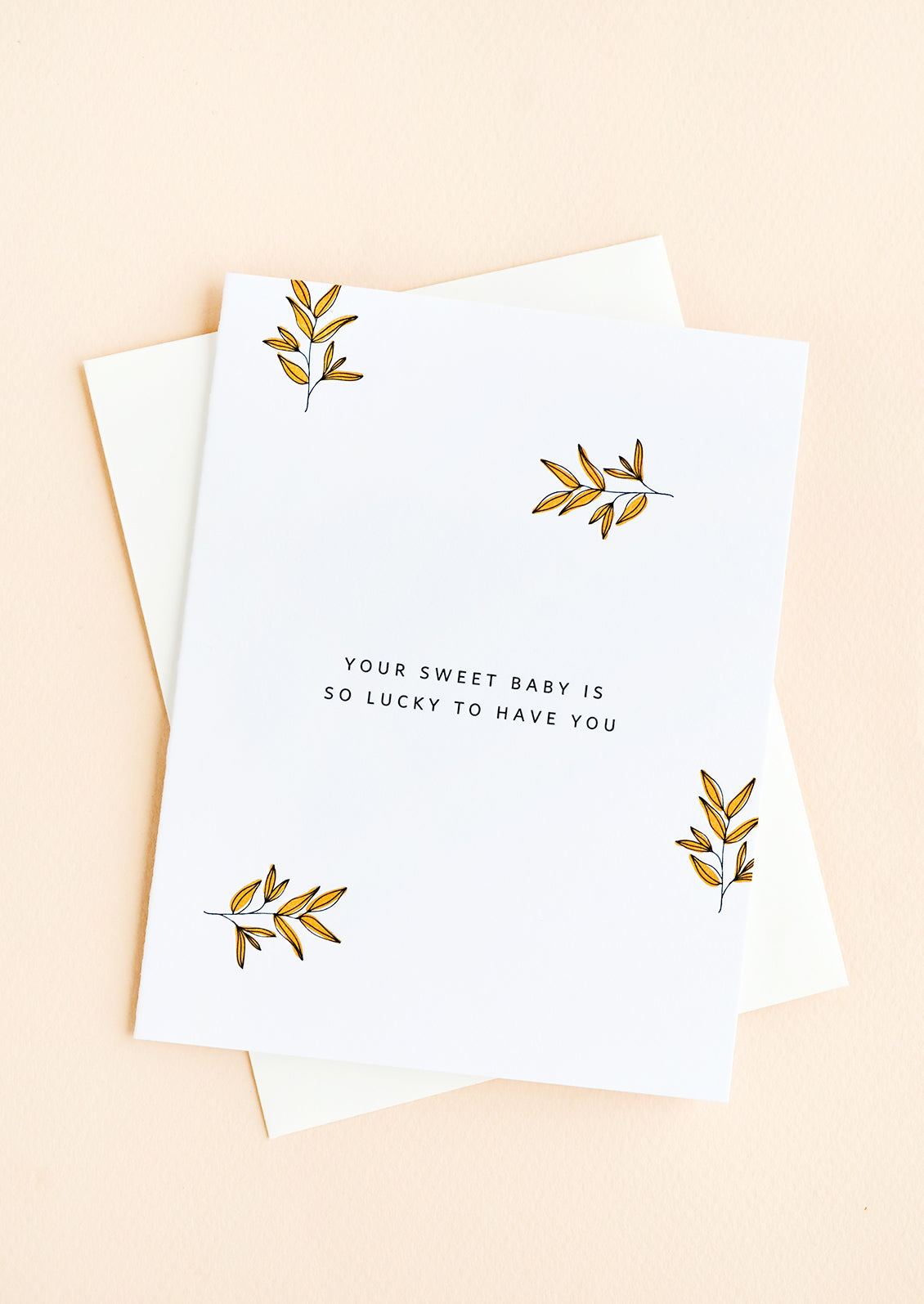 A greeting card with scattered leaf print and small caps text reading "Your sweet baby is so lucky to have you"
