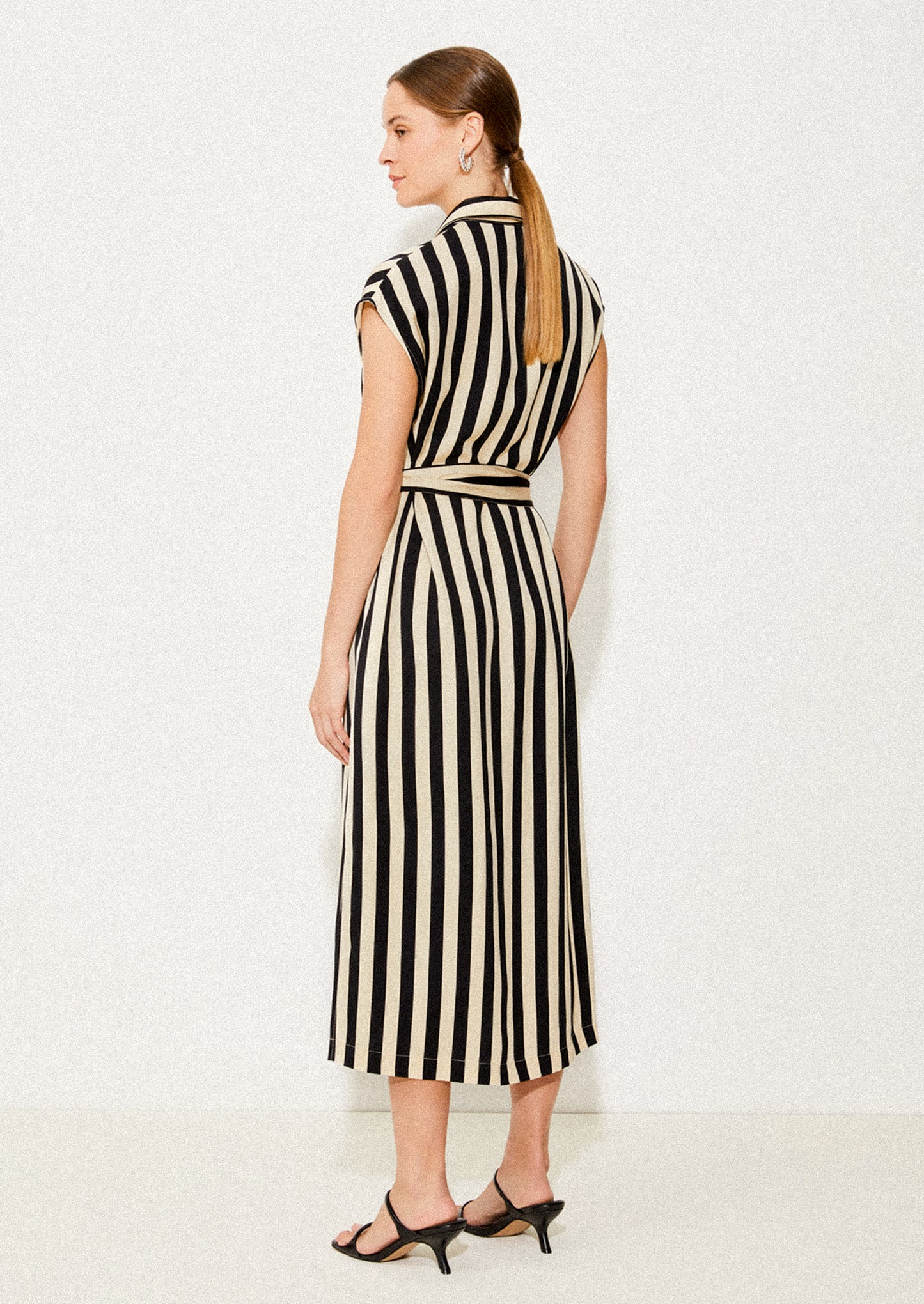 A woman wearing a sleeveless collared dress in vertical black and ivory stripes.