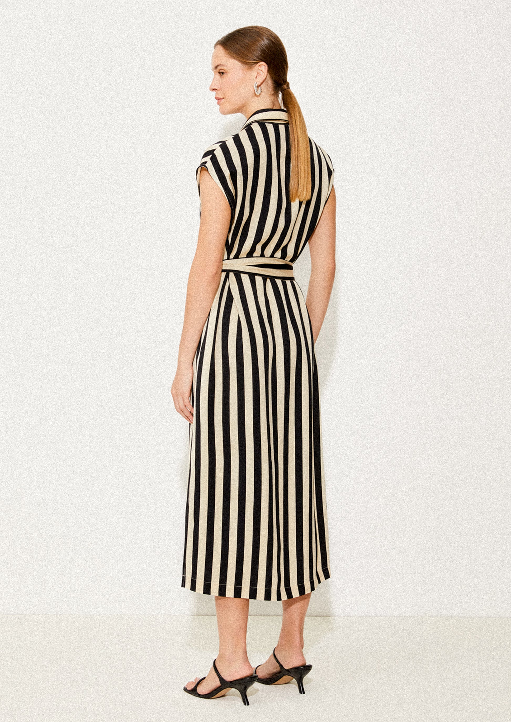 A woman wearing a sleeveless collared dress in vertical black and ivory stripes.