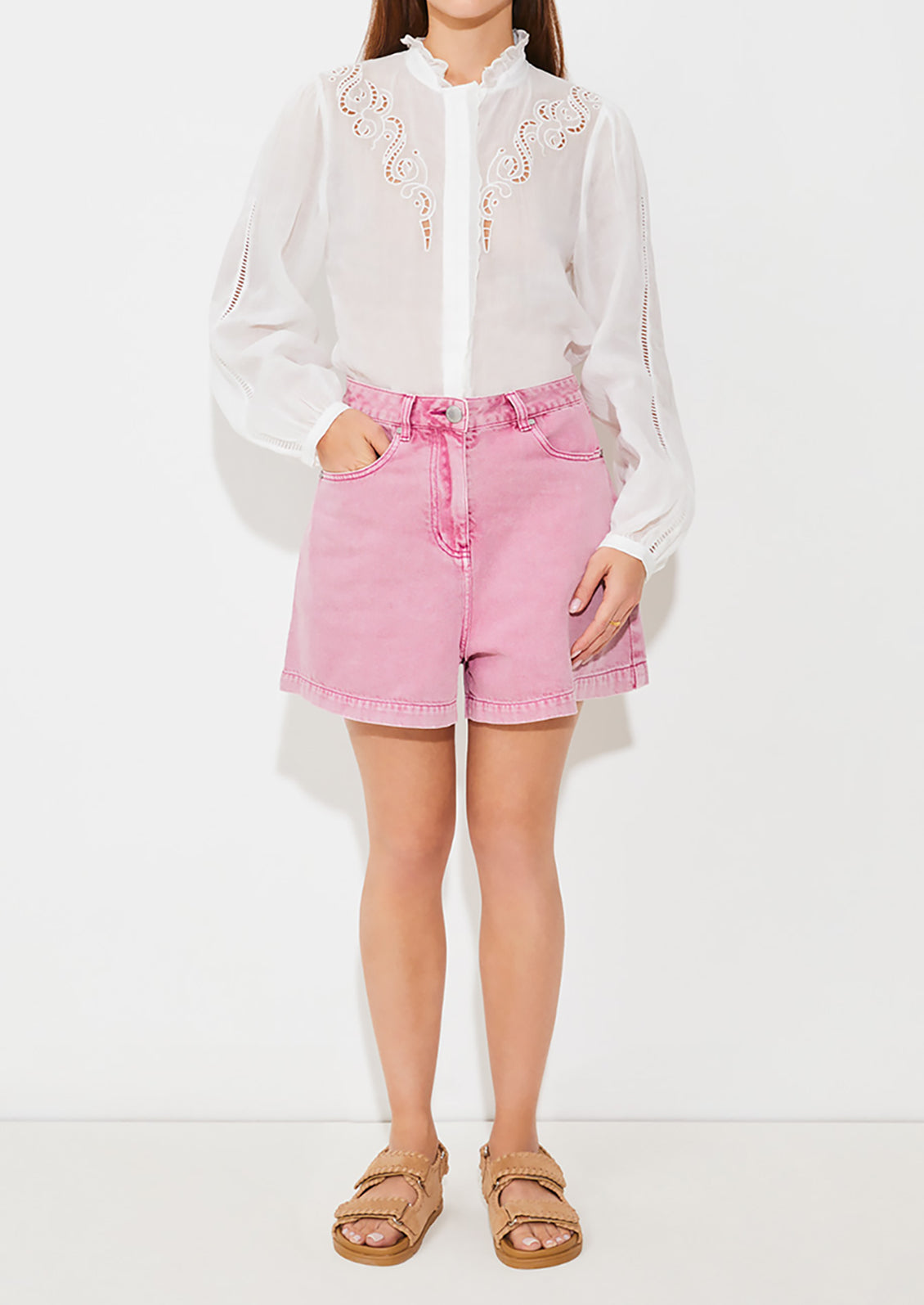 A person wearing a pair of high waisted denim shorts in pink overdye wash.