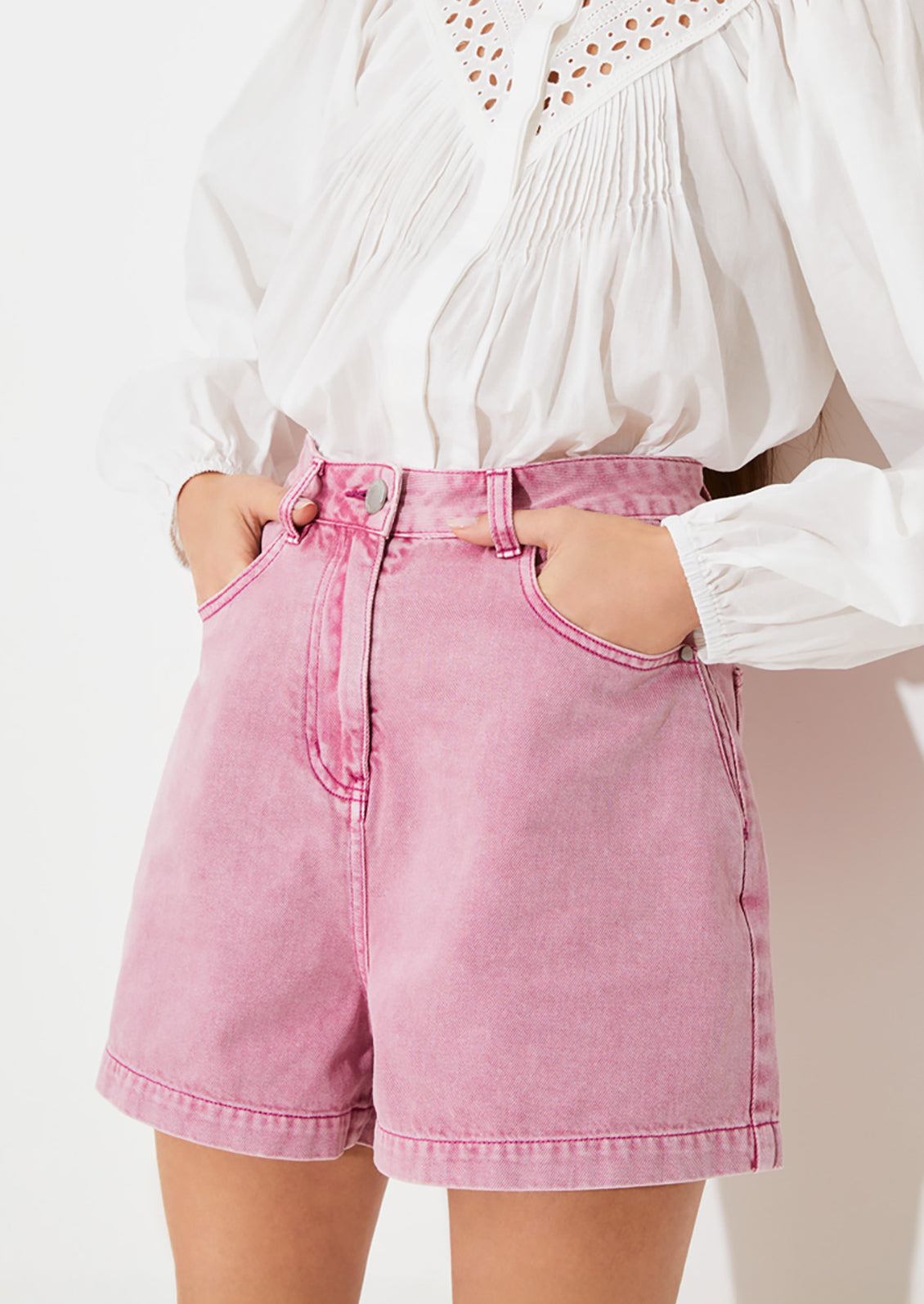 A person wearing a pair of high waisted denim shorts in pink overdye wash.