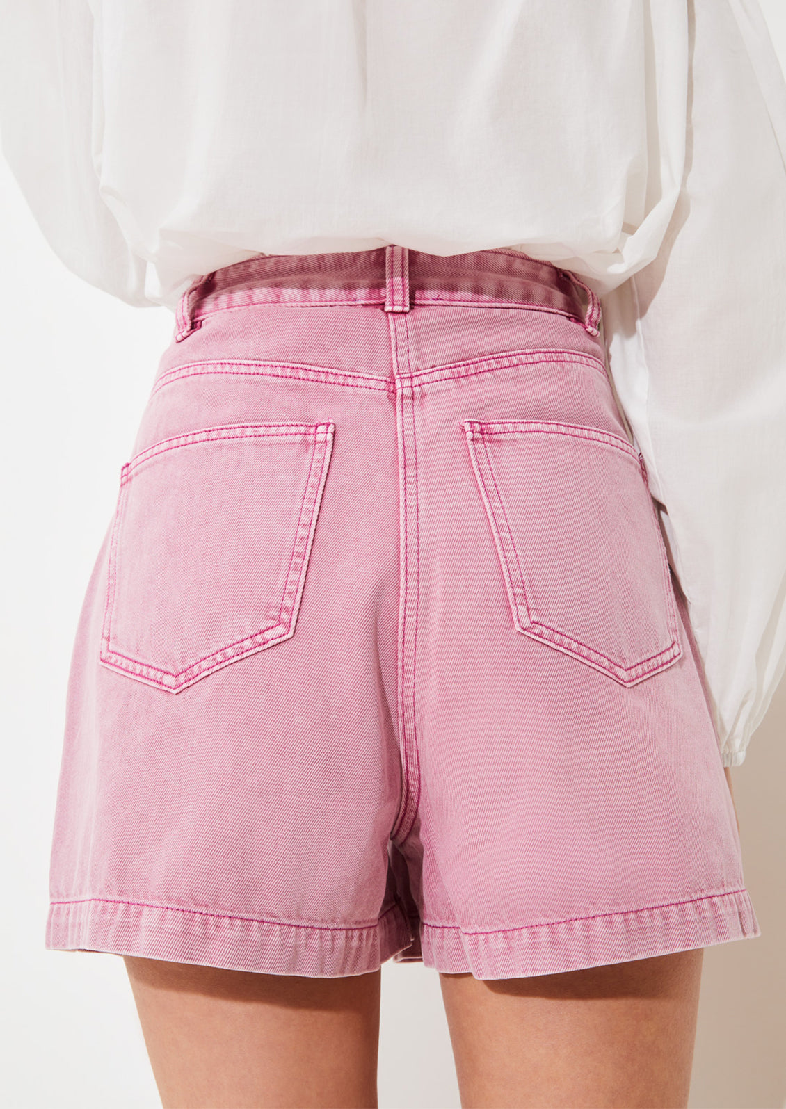 A person wearing a pair of high waisted denim shorts in pink overdye wash.