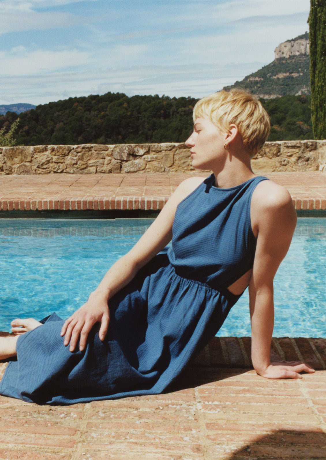 A woman wearing a blue sleeveless dress with cutouts at side waist.