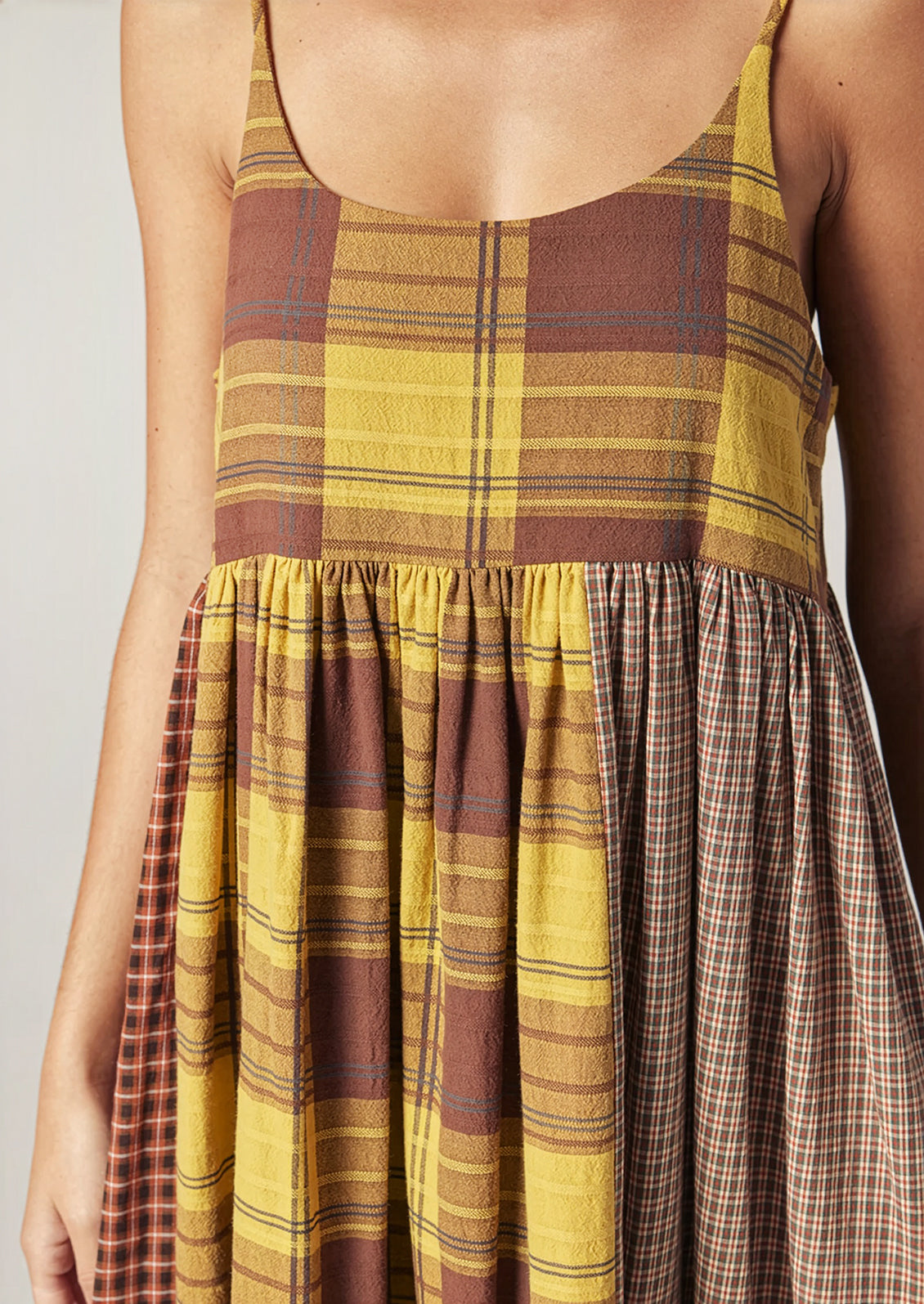 A person wearing a long plaid cotton dress in brown and yellow tones.
