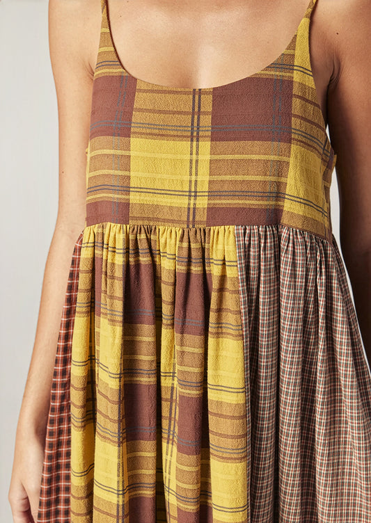 A person wearing a long plaid cotton dress in brown and yellow tones.