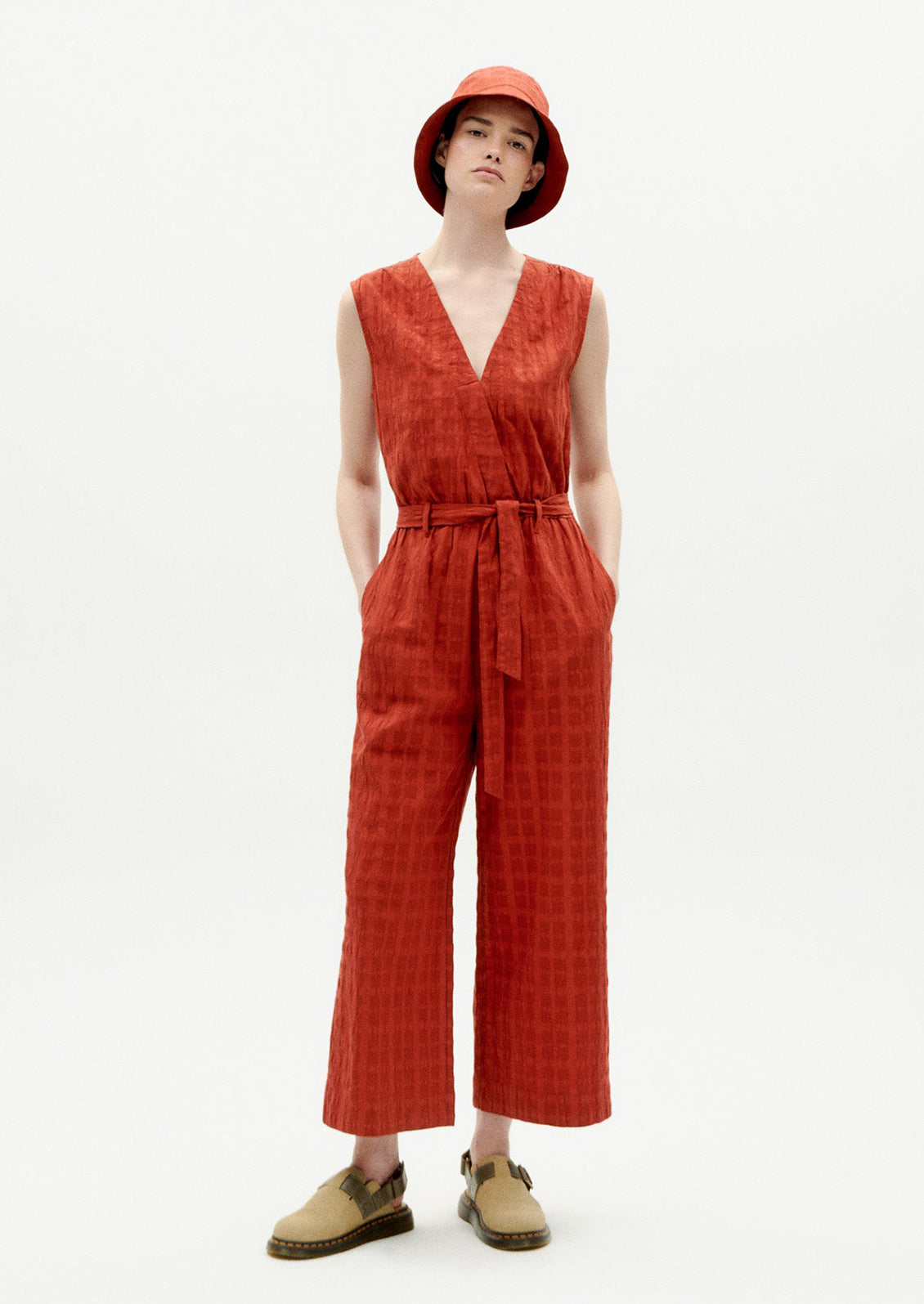 A woman wearing a rust colored jumpsuit with tie waist and tonal grid texture.