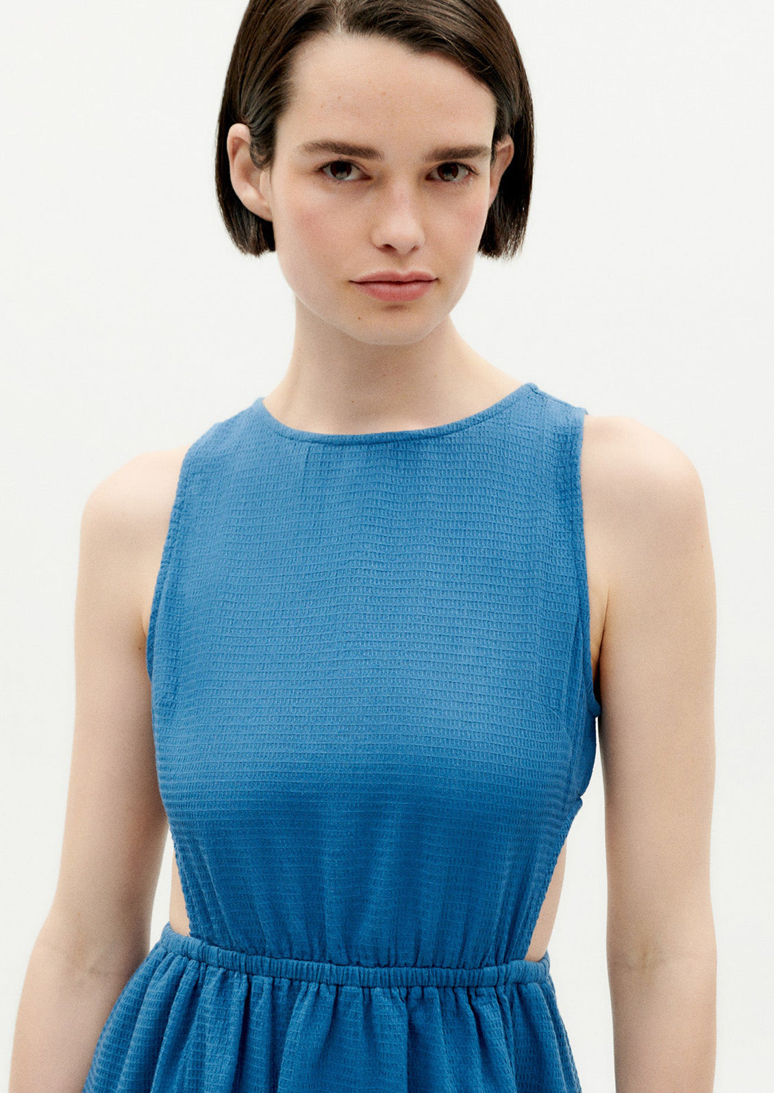 A woman wearing a blue sleeveless dress with cutouts at side waist.