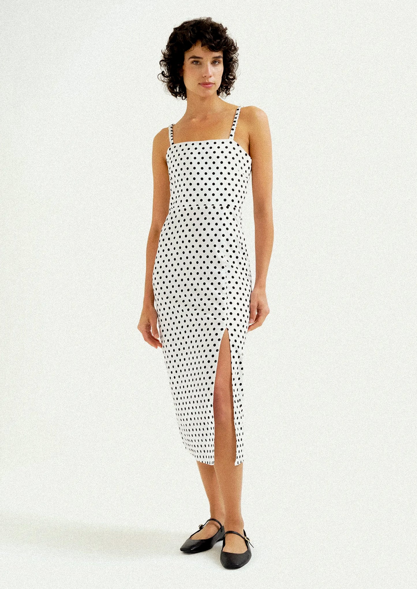 A woman wearing a midi dress in white with black polka dots.