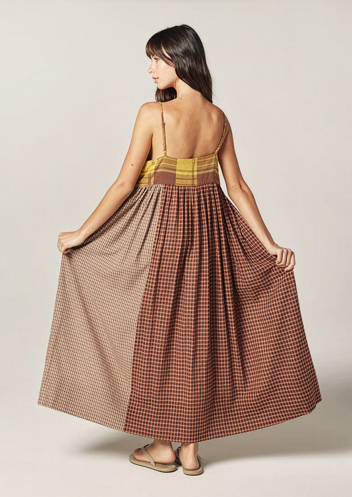 A person wearing a long plaid cotton dress in brown and yellow tones.
