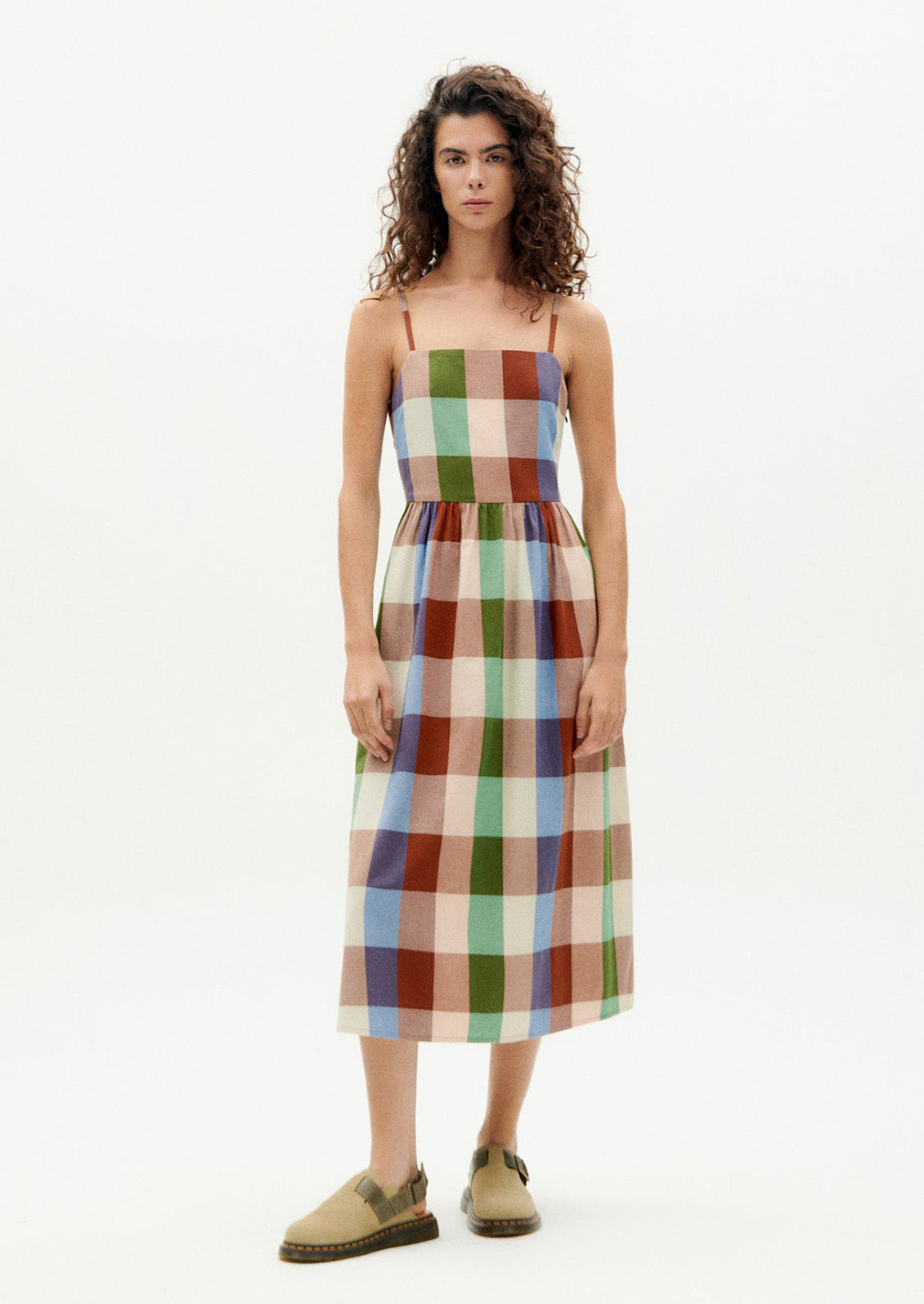 A woman wearing a thin strap dress with straight neckline, in colorful madras cotton.