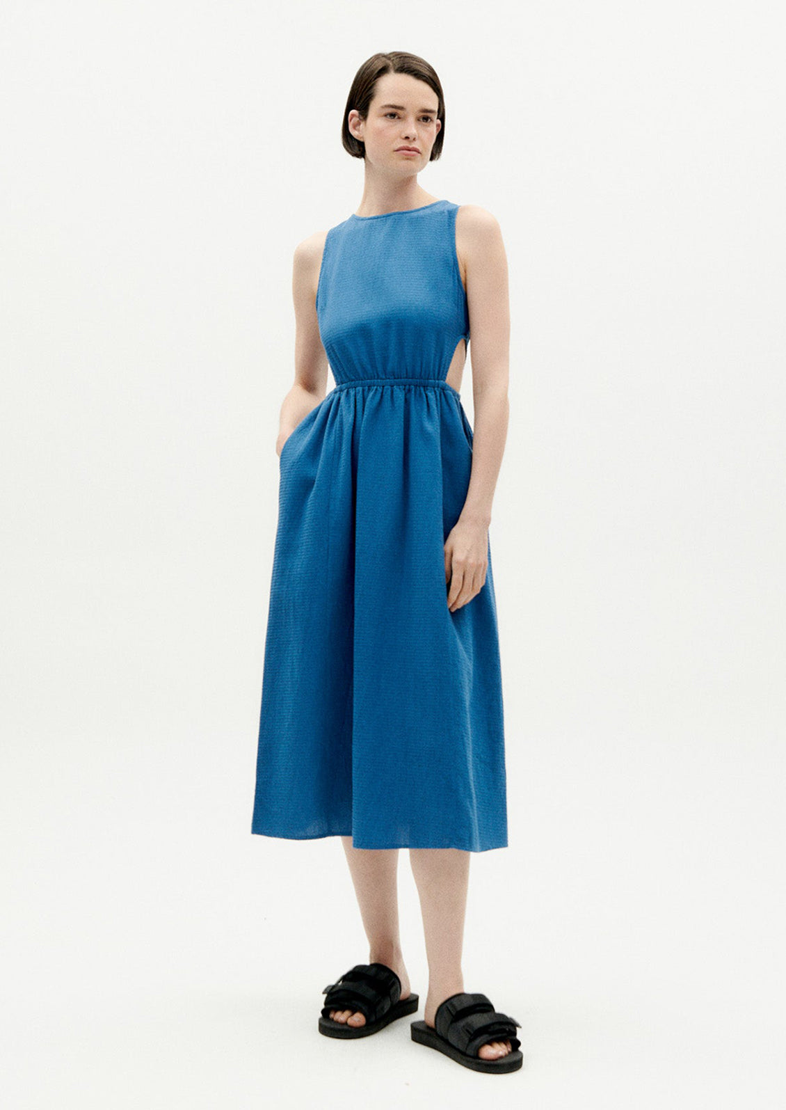 A woman wearing a blue sleeveless dress with cutouts at side waist.