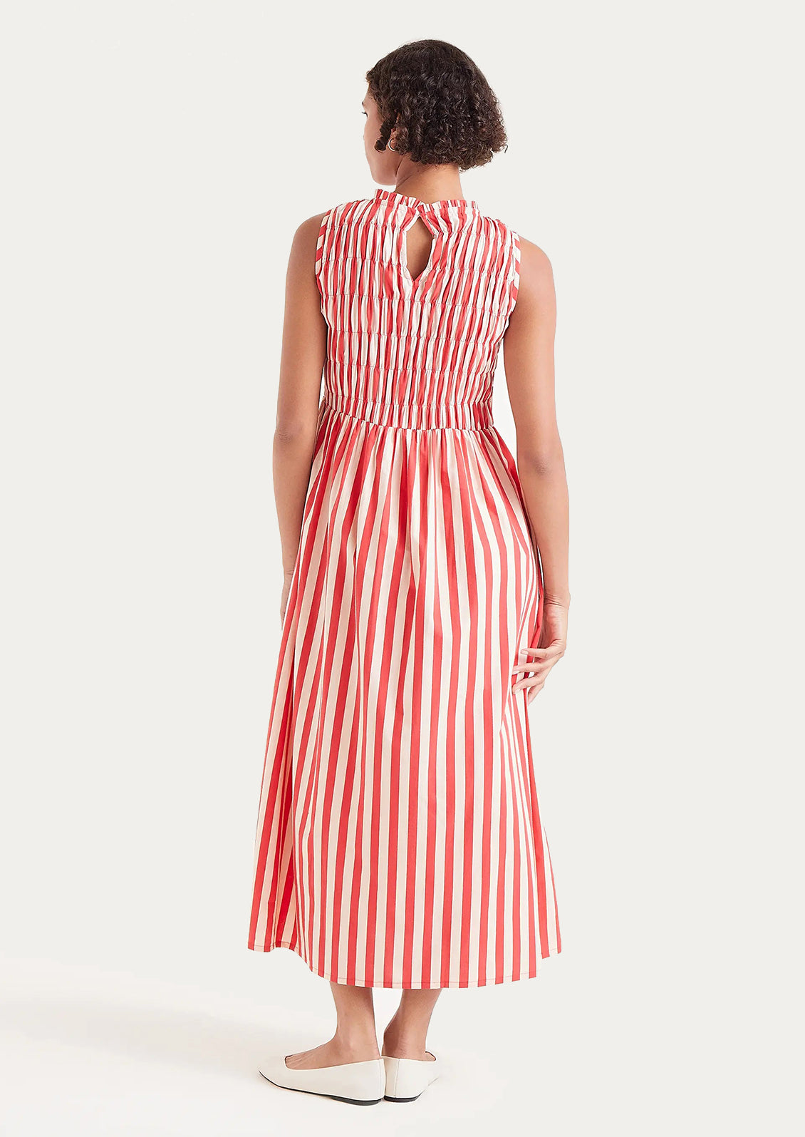 A woman wearing a cotton dress with smocked bodice in vertical red stripes.