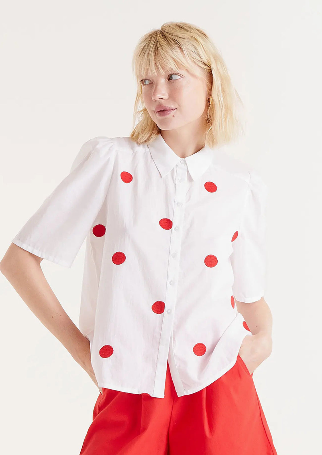 A woman wearing a short sleeve cotton blouse with slight puff sleeve and embroidered red dot pattern.