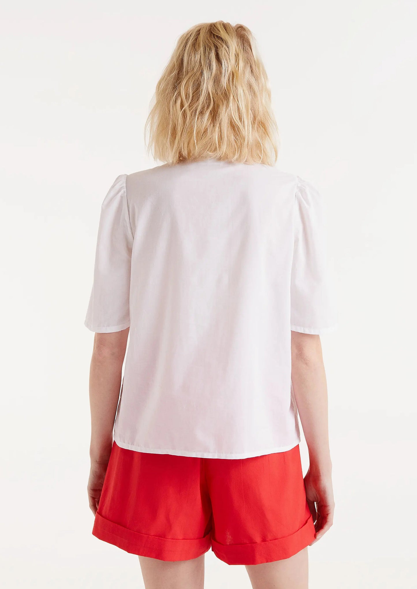 A woman wearing a short sleeve cotton blouse with slight puff sleeve and embroidered red dot pattern.