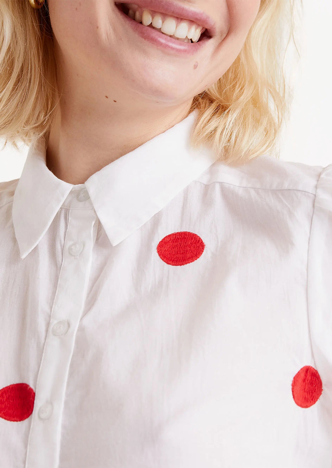 A woman wearing a short sleeve cotton blouse with slight puff sleeve and embroidered red dot pattern.