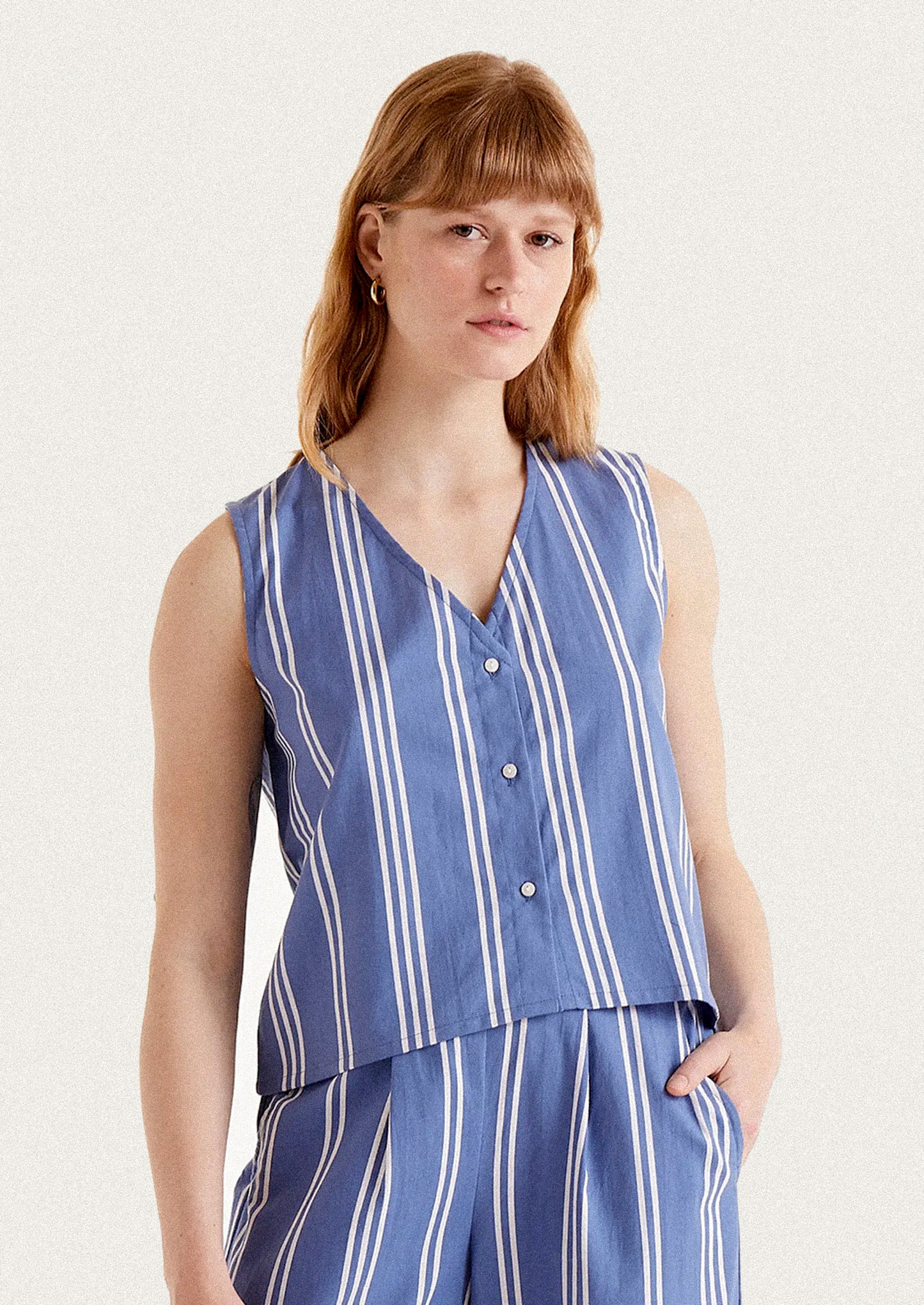 A woman wearing a v-neck button front top in blue with white vertical stripes.