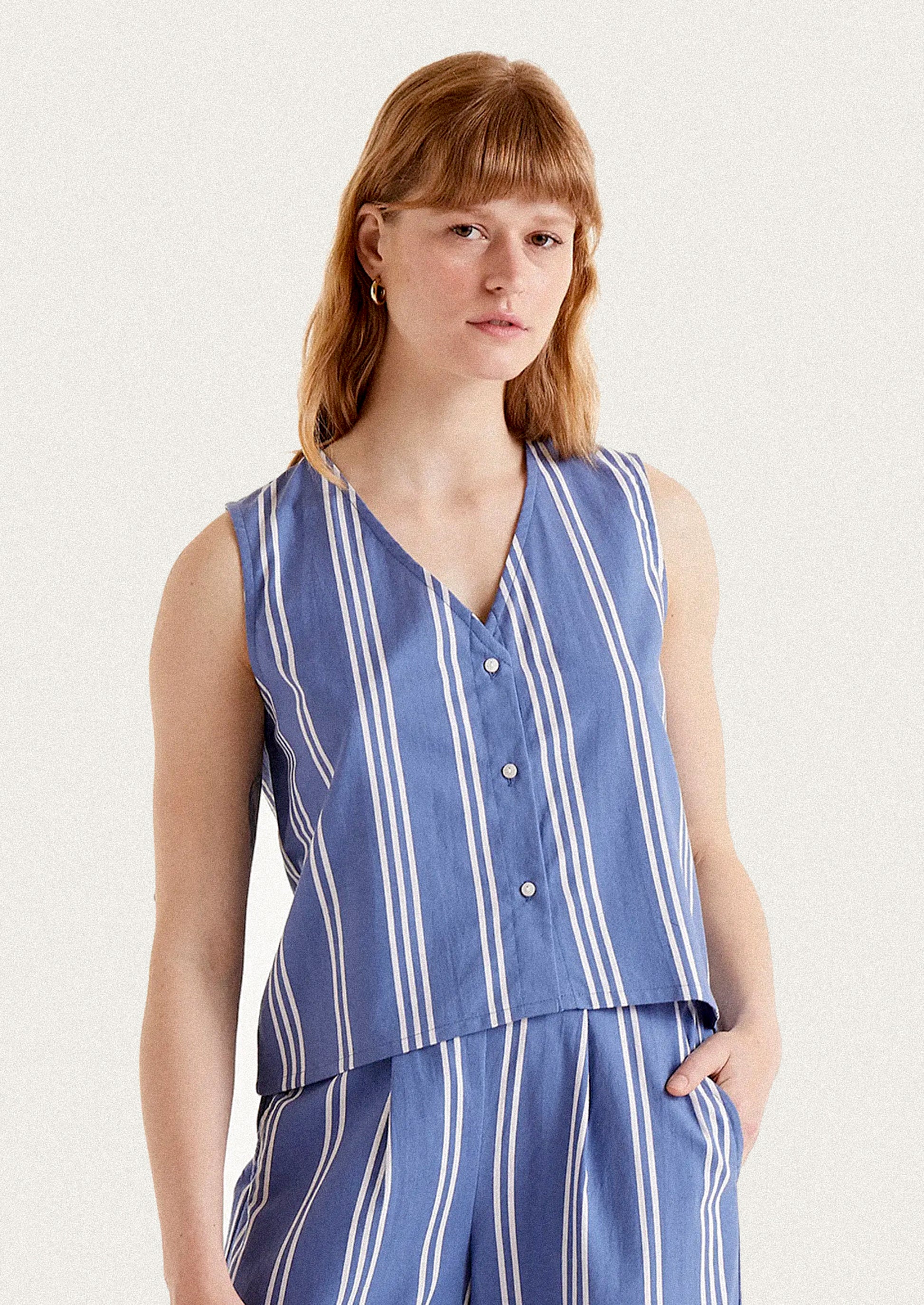 A woman wearing a v-neck button front top in blue with white vertical stripes.