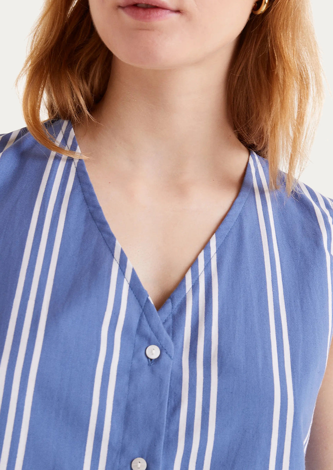 A woman wearing a v-neck button front top in blue with white vertical stripes.