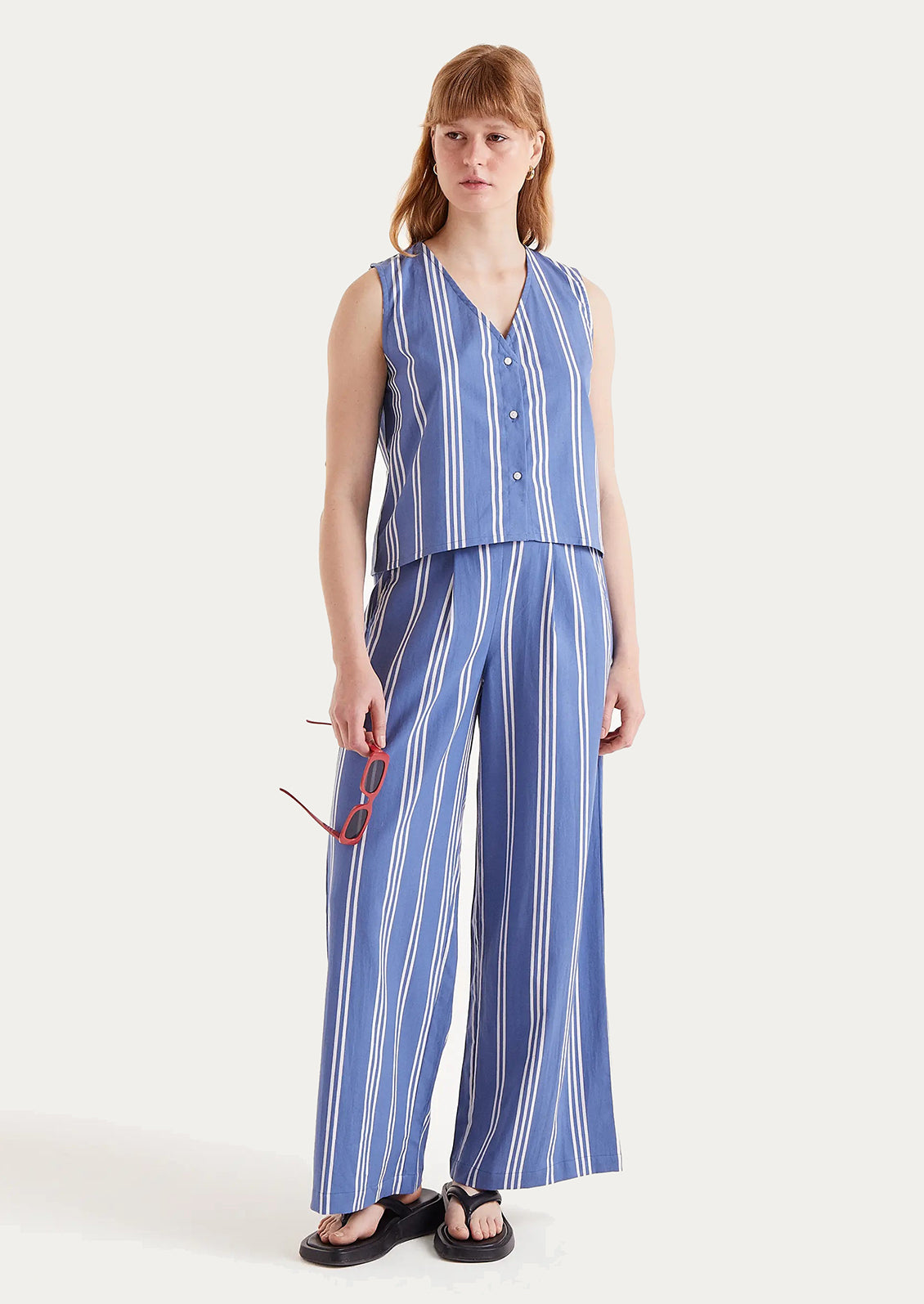 A woman wearing a v-neck button front top in blue with white vertical stripes.