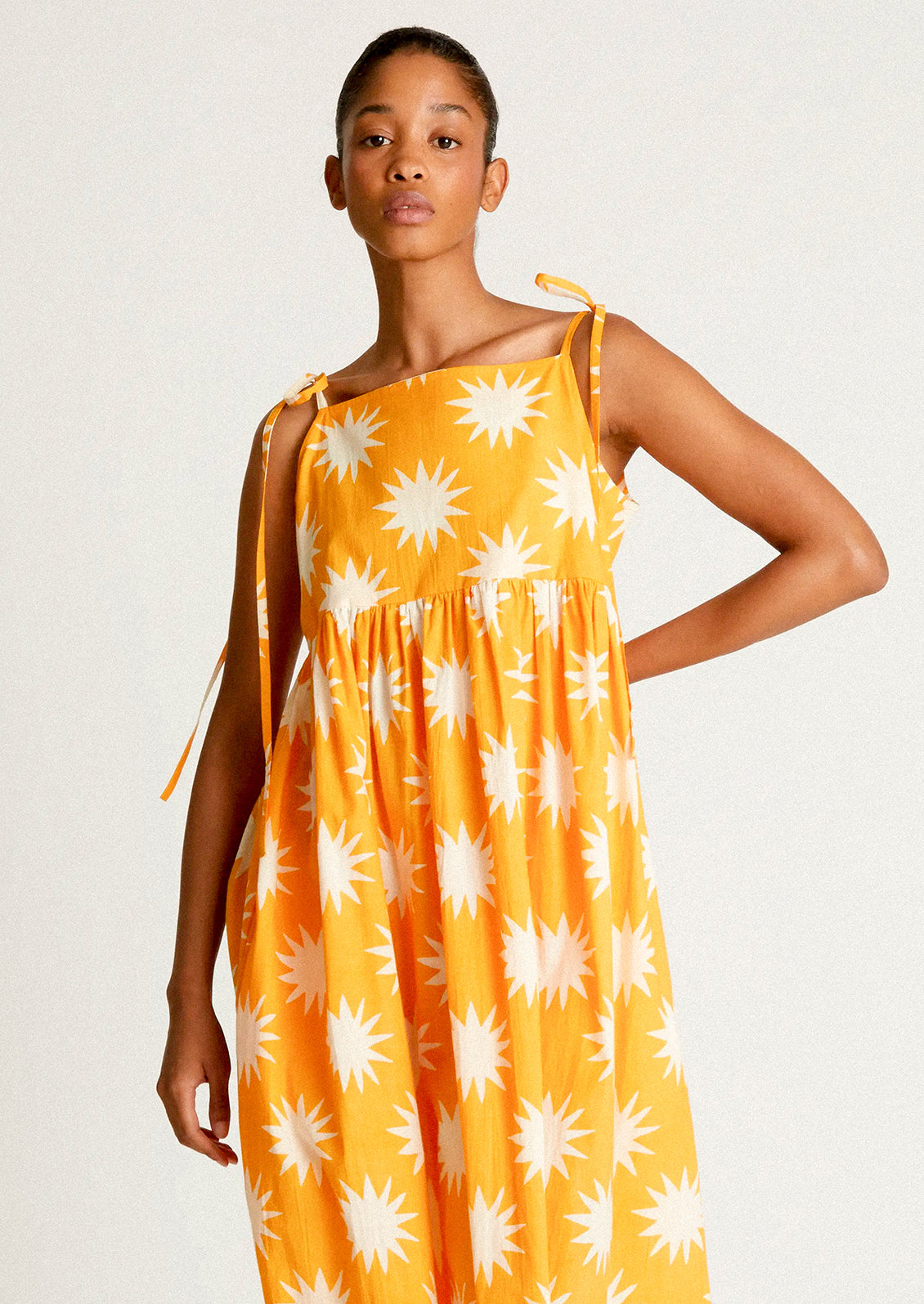 A woman wearing a yellow tie shoulder dress with big sun pattern in white.