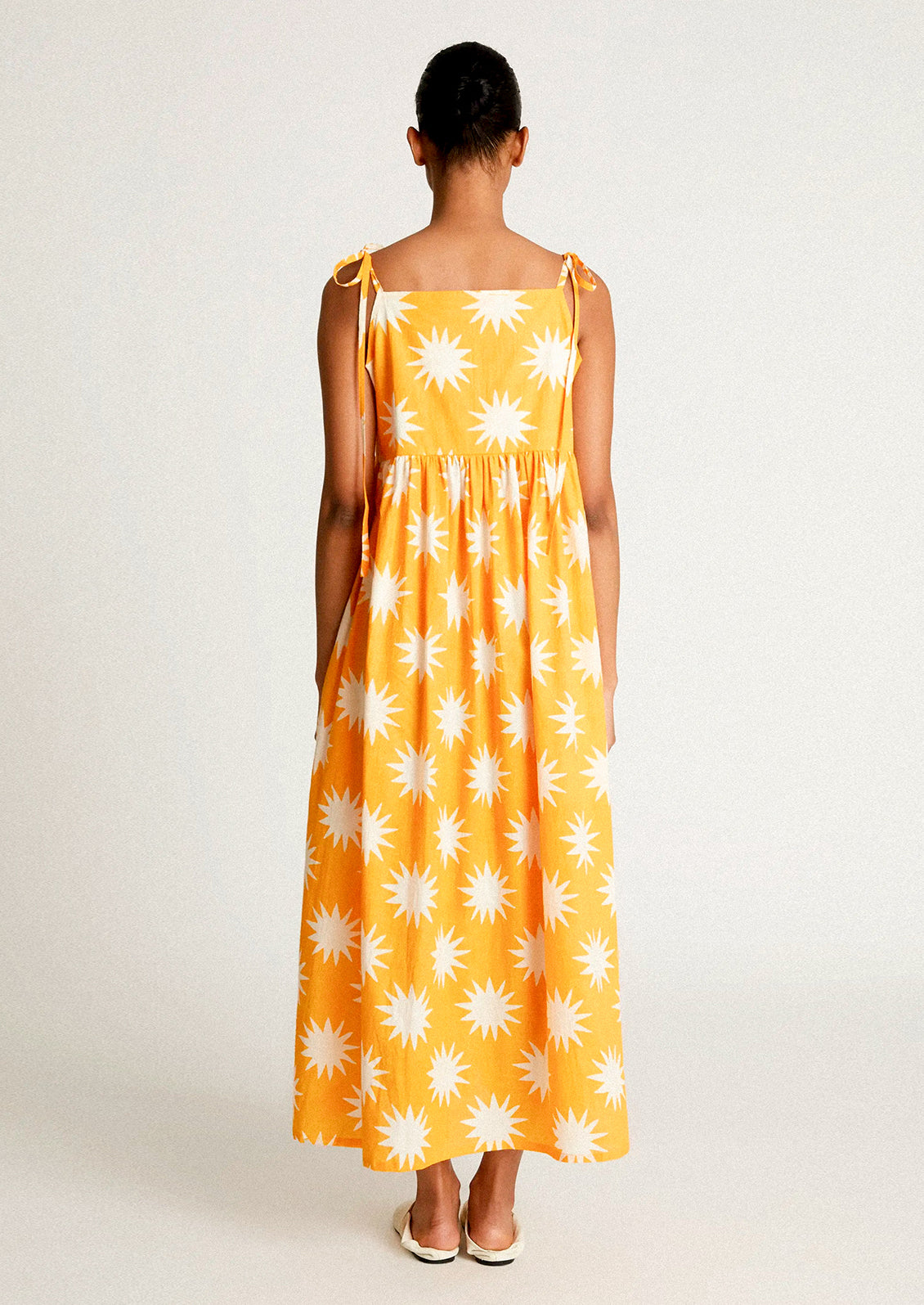 A woman wearing a yellow tie shoulder dress with big sun pattern in white.