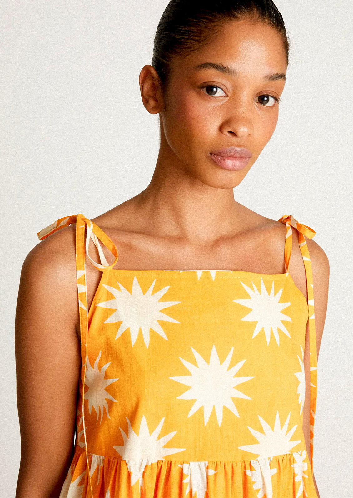A woman wearing a yellow tie shoulder dress with big sun pattern in white.