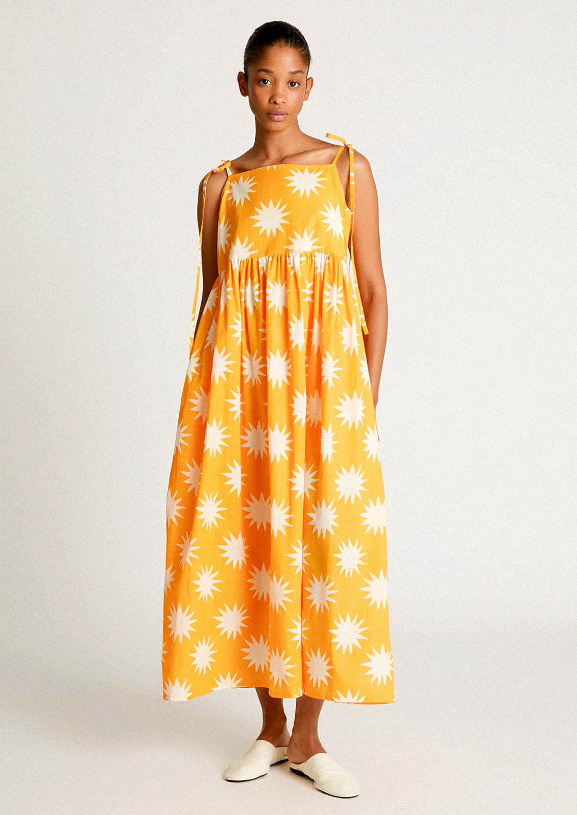 A woman wearing a yellow tie shoulder dress with big sun pattern in white.