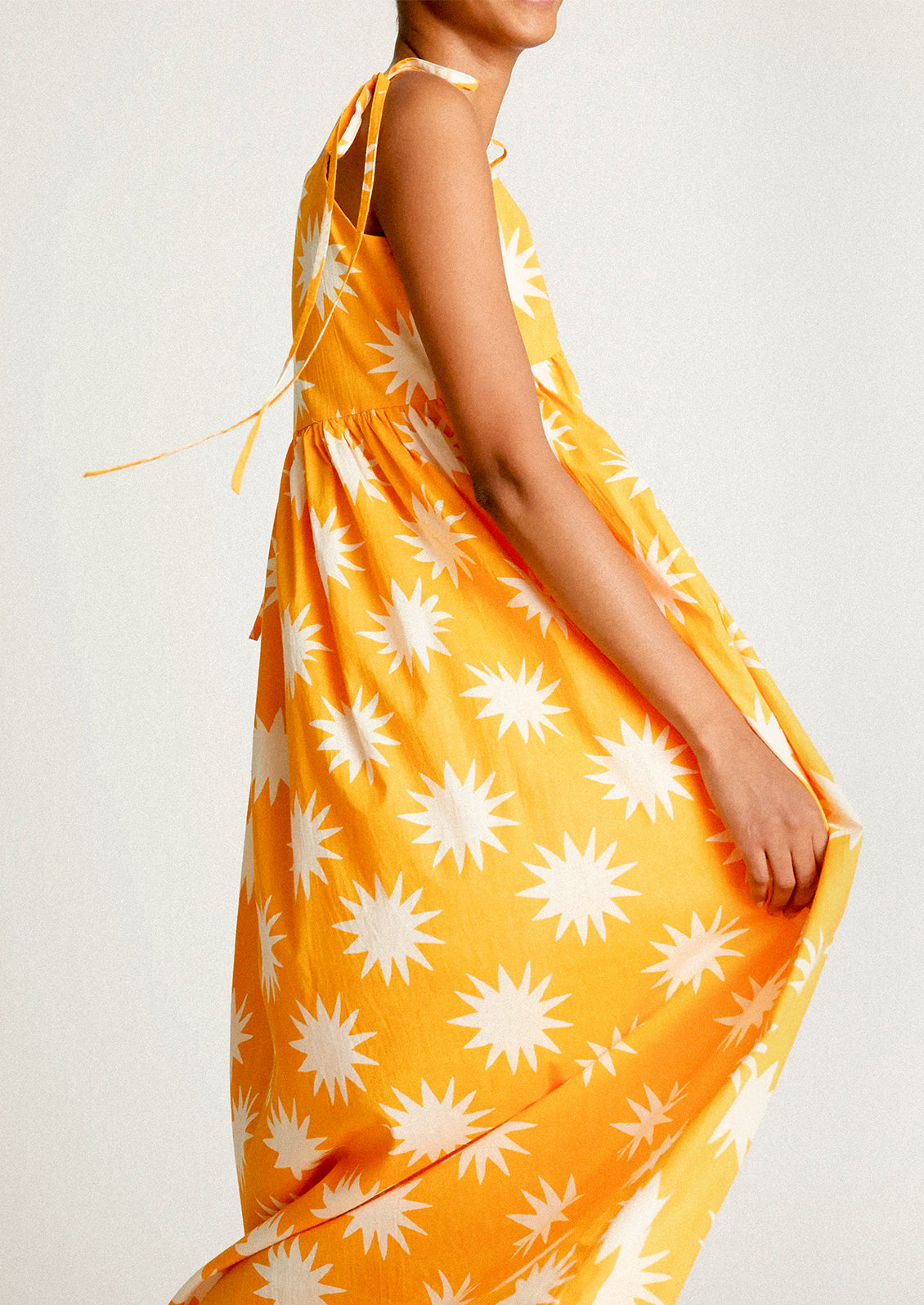 A woman wearing a yellow tie shoulder dress with big sun pattern in white.