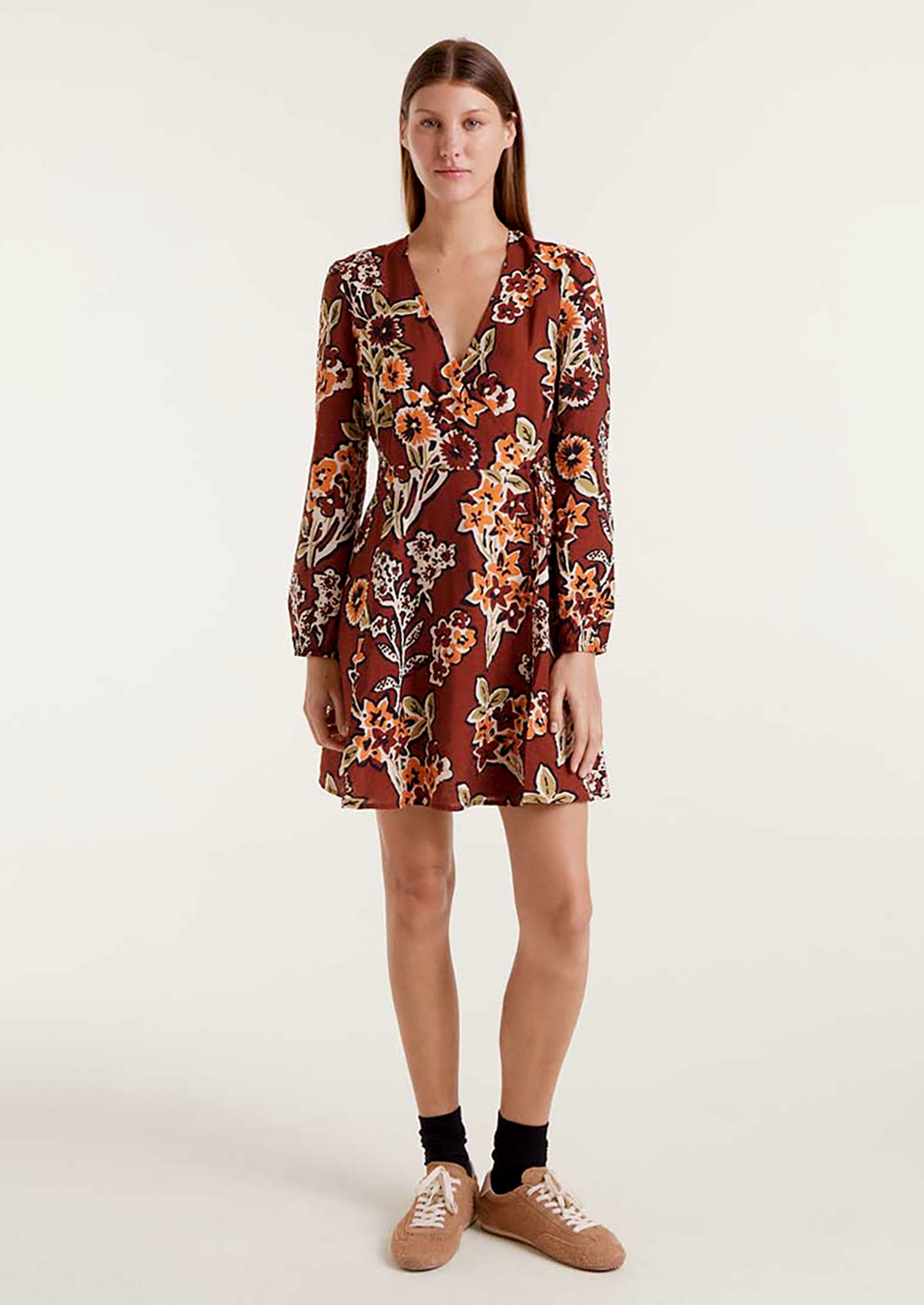 A woman wearing a brown mini long sleeve dress with orange and green floral pattern.