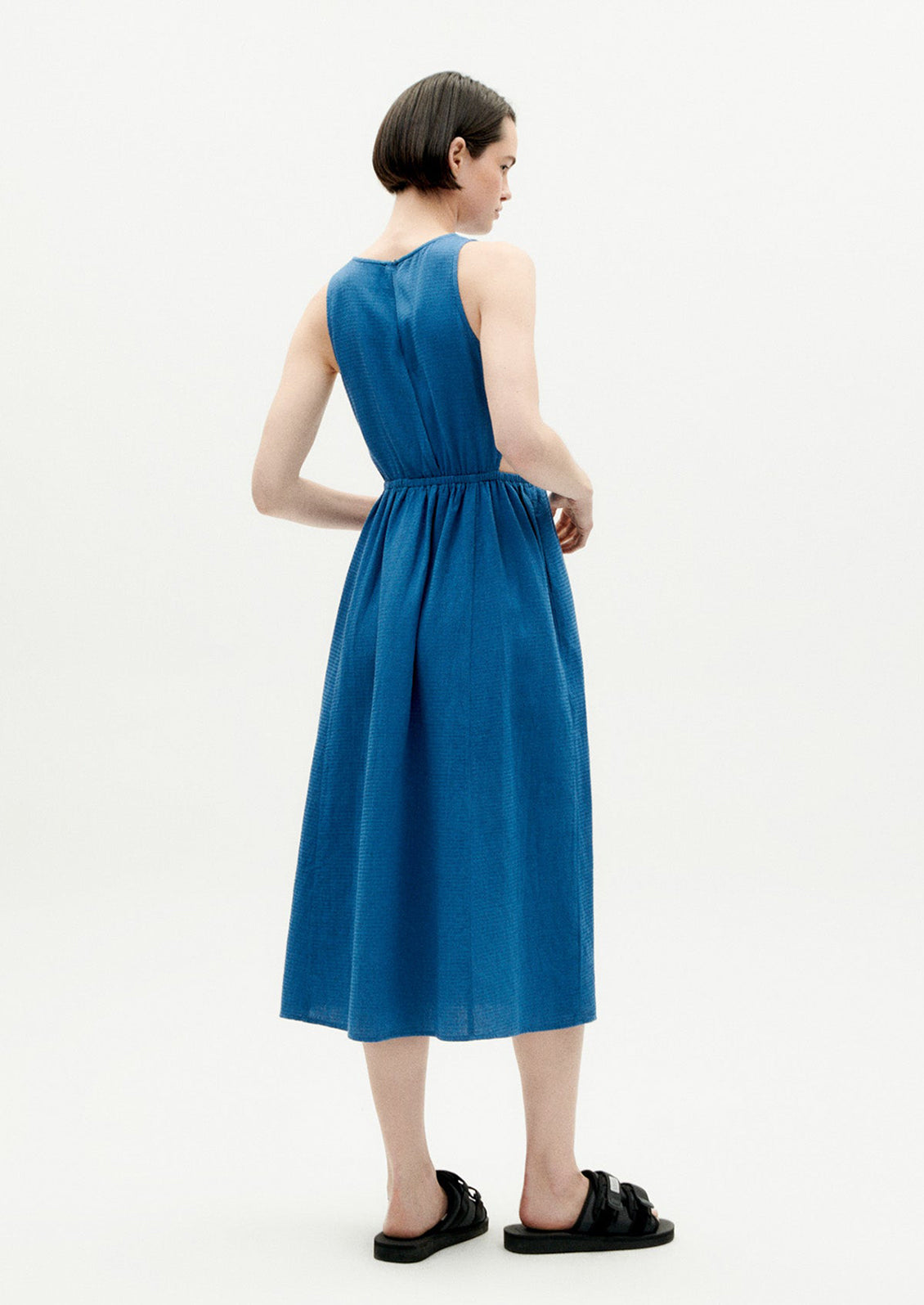 A woman wearing a blue sleeveless dress with cutouts at side waist.