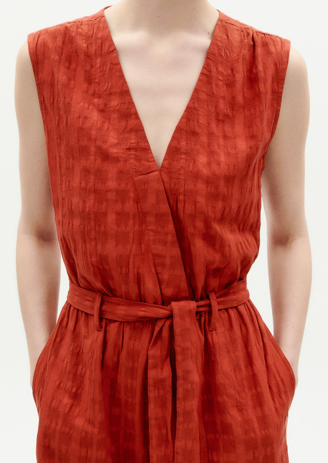 A woman wearing a rust colored jumpsuit with tie waist and tonal grid texture.