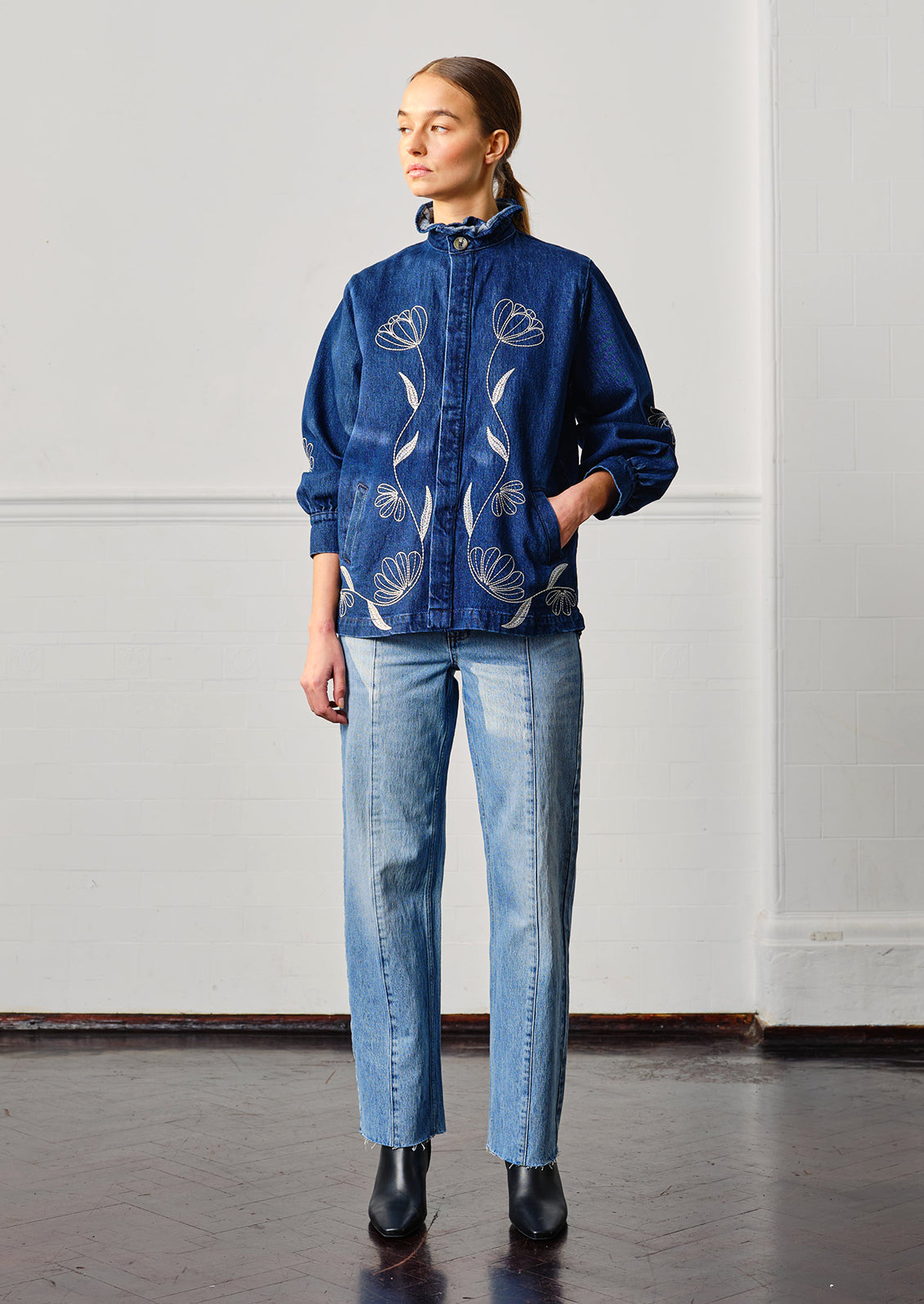A woman wearing a blue denim jacket with white floral embroidery.